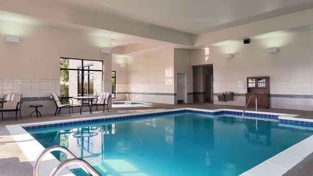 Une piscine intérieure à l’eau d’un bleu limpide, entourée de chaises longues et d’une petite table.