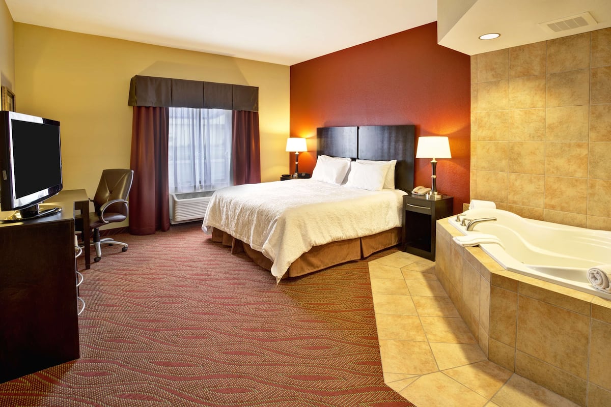 Une chambre d’hôtel comprenant un lit, un bureau avec une télévision, une chaise, une salle de bain avec une baignoire et une fenêtre avec des rideaux.