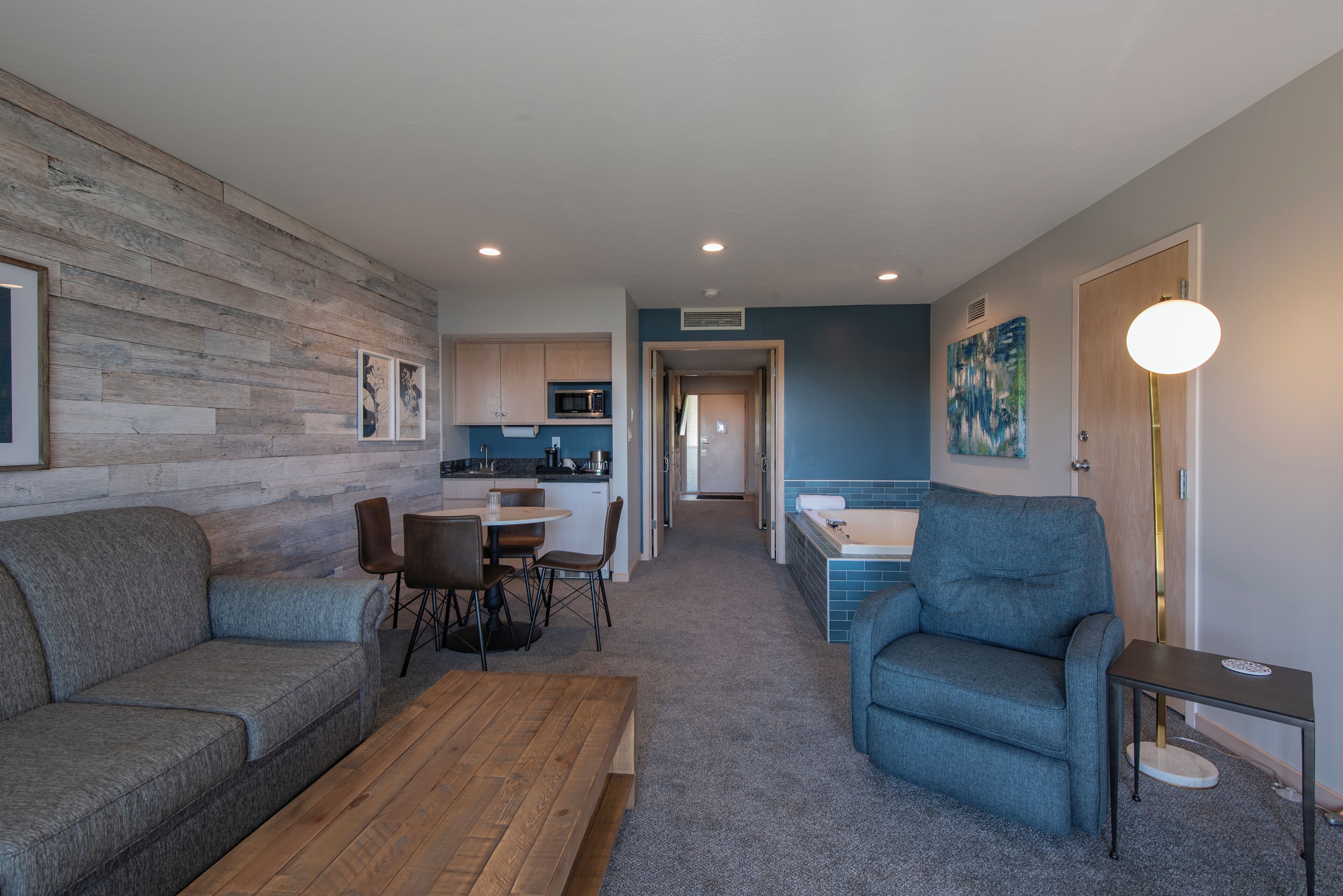 A modern living room with a wooden accent wall, a dining area with a table and chairs, a blue armchair, and a small side table.
