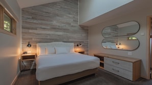 A modern bedroom with a large bed, a nightstand, a dresser, and a wall-mounted mirror. - Country House Resort (Sister Bay)