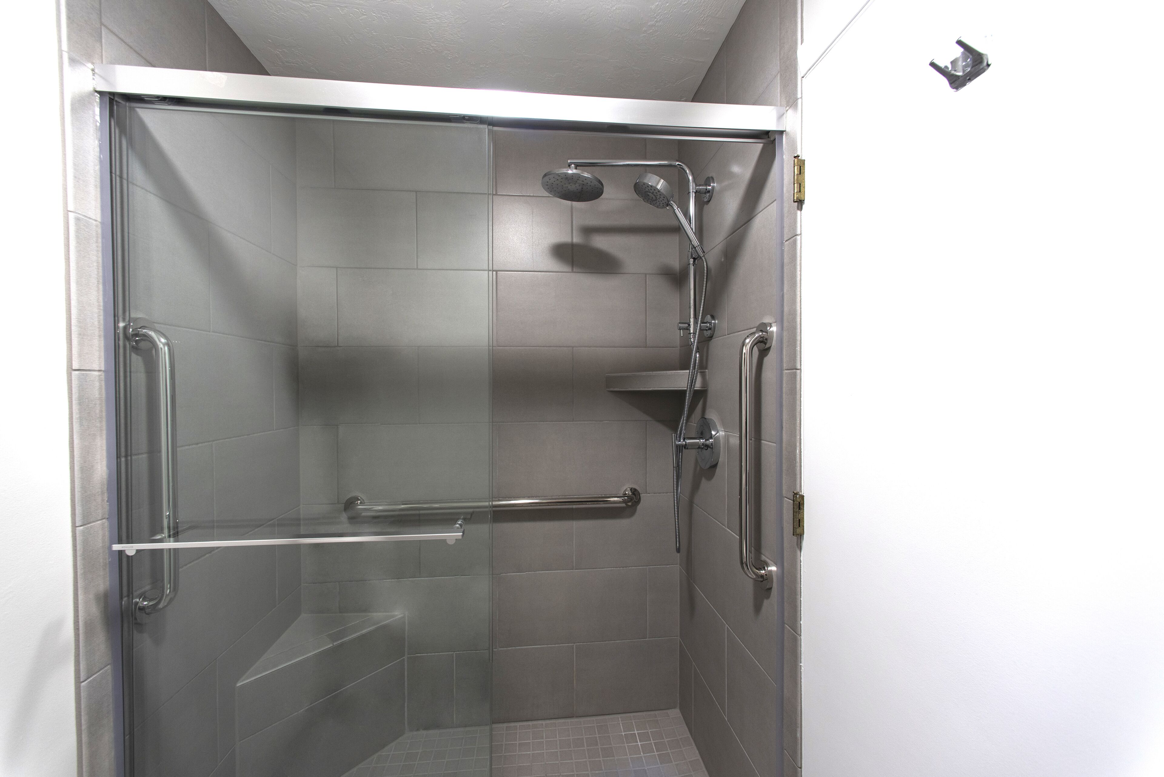 A modern shower with a glass door, a handheld showerhead, a wall-mounted faucet, and a grab bar for safety.