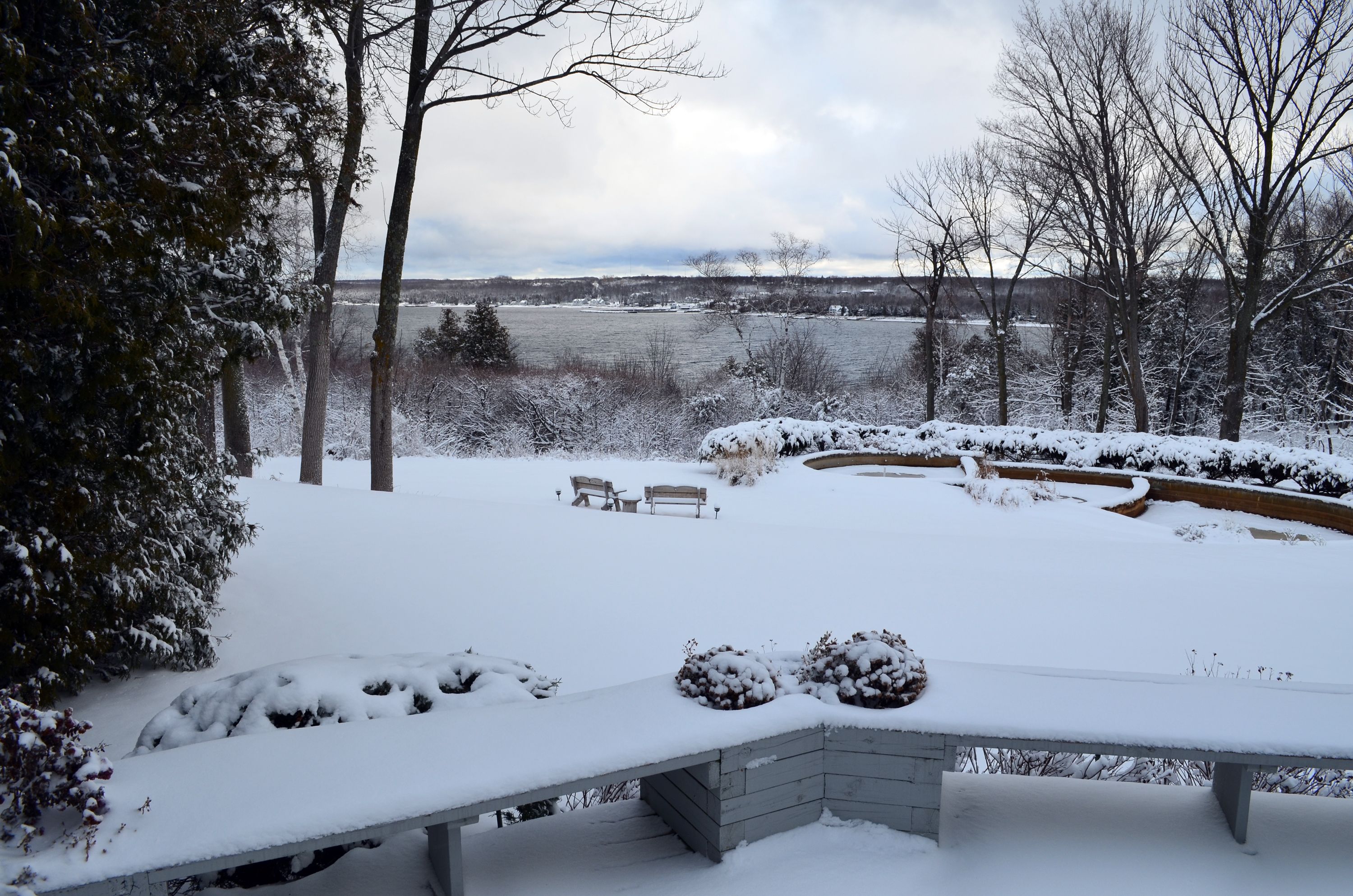 A snow-covered outdoor area with a bench, a small table, and a circular garden bed.