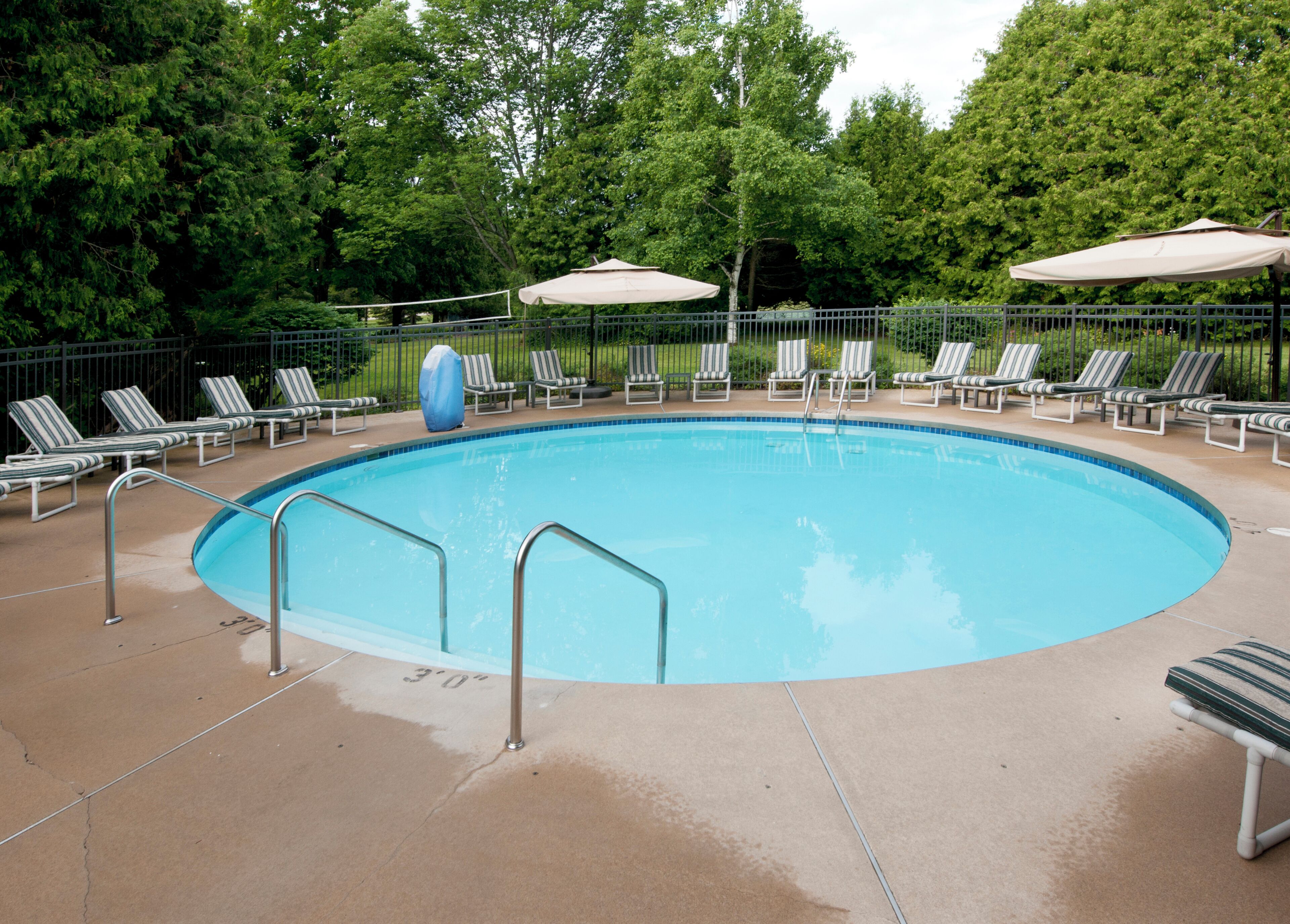 A circular pool with a surrounding deck, lounge chairs, and umbrellas.