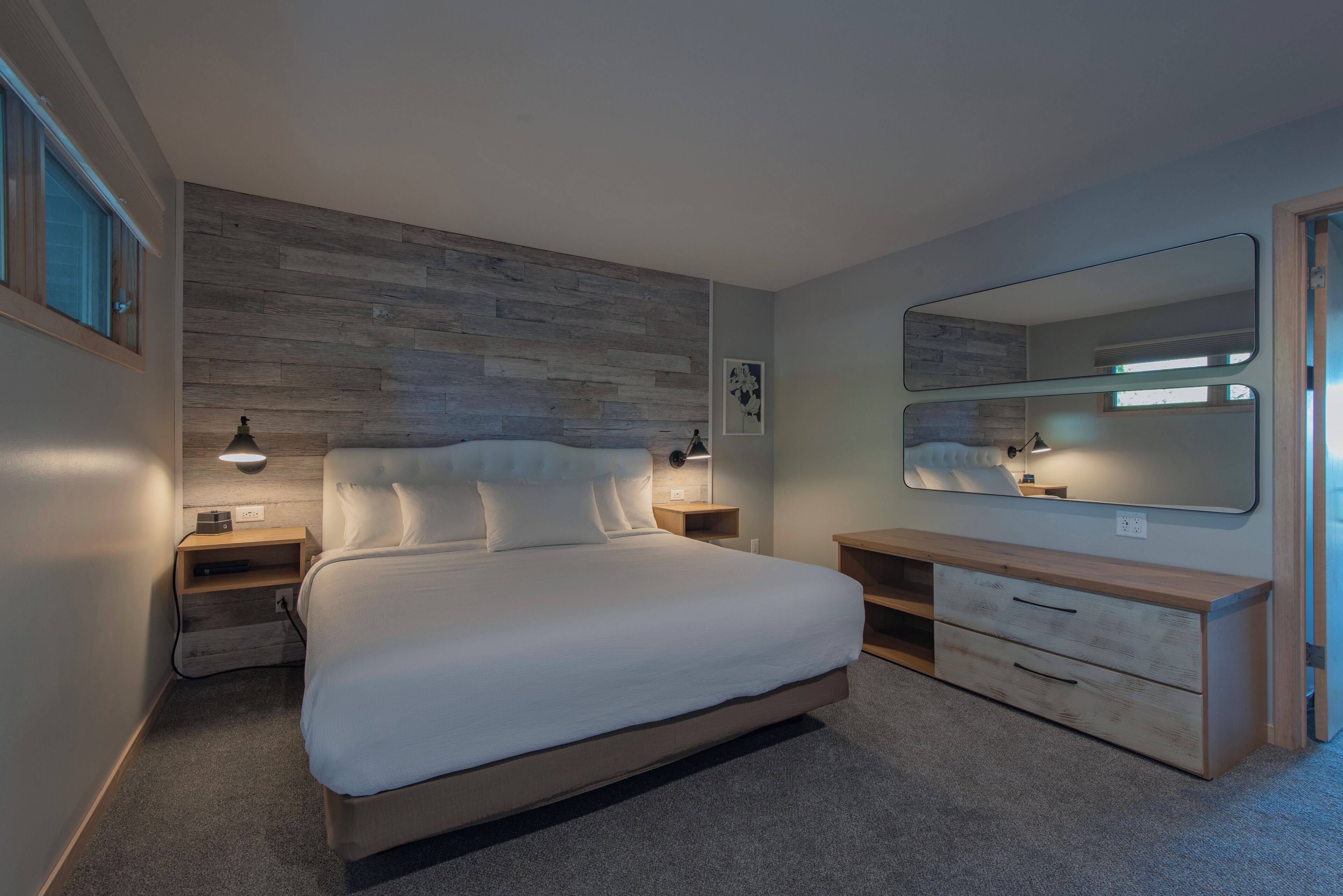 Quarto moderno com uma cama grande, mesas de cabeceira, cômoda e um espelho amplo.
