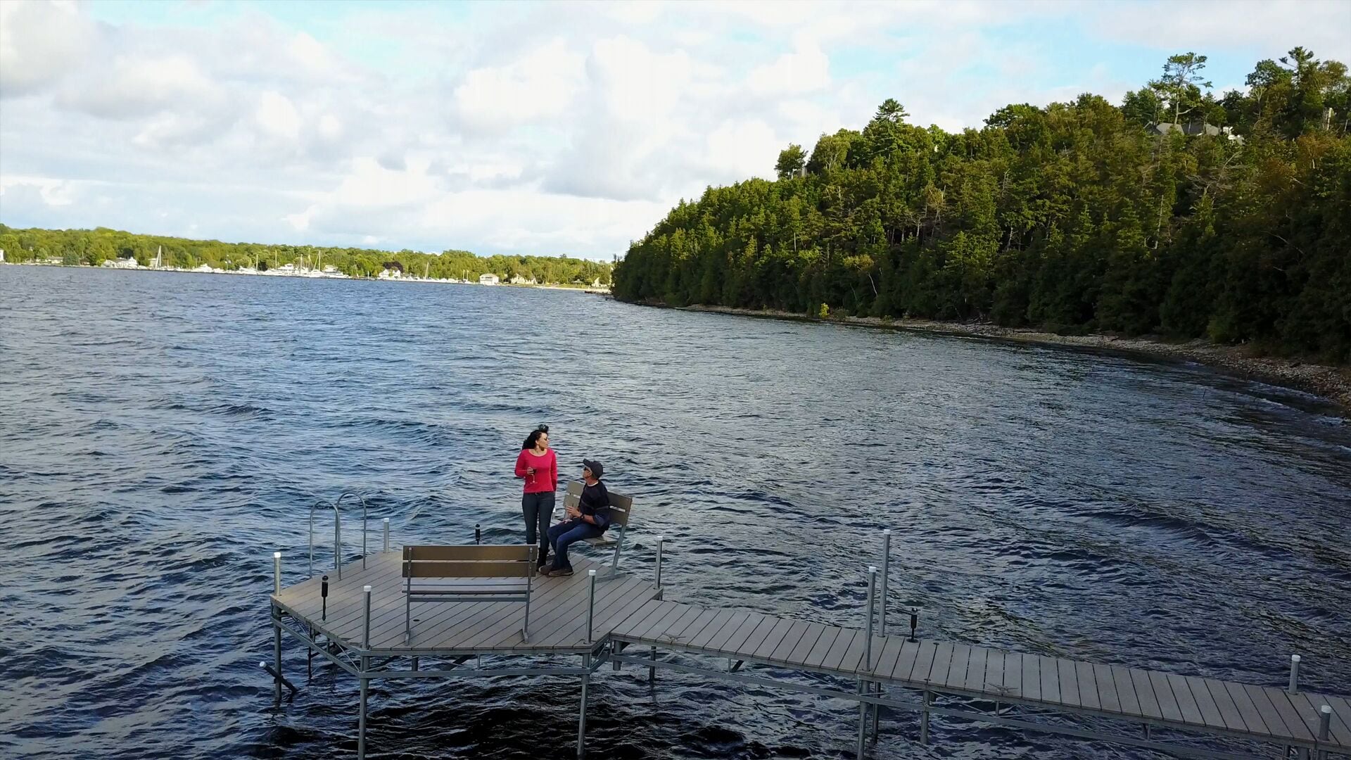Une jetée en bois s’étendant dans une étendue d’eau, avec une rive boisée en arrière-plan.
