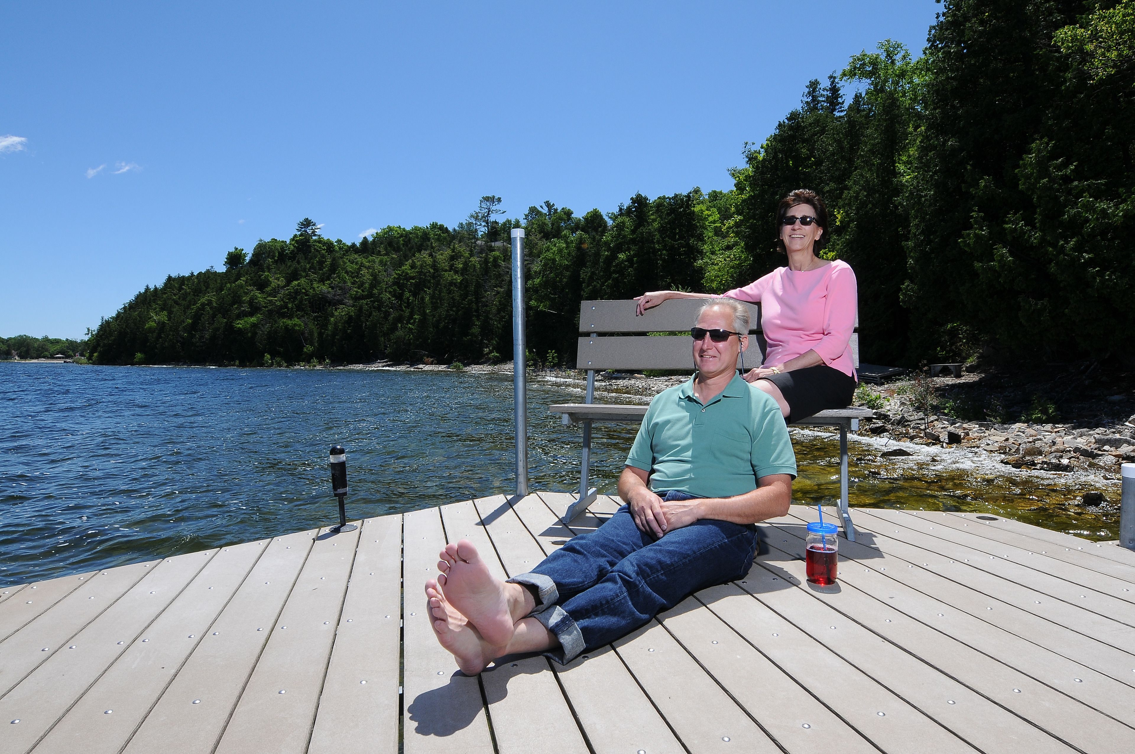 A wooden dock with a bench and a table, overlooking a calm body of water and a forested shoreline.