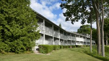 Un hotel a più piani con un balcone su ogni piano, circondato da prati curati e alberi.