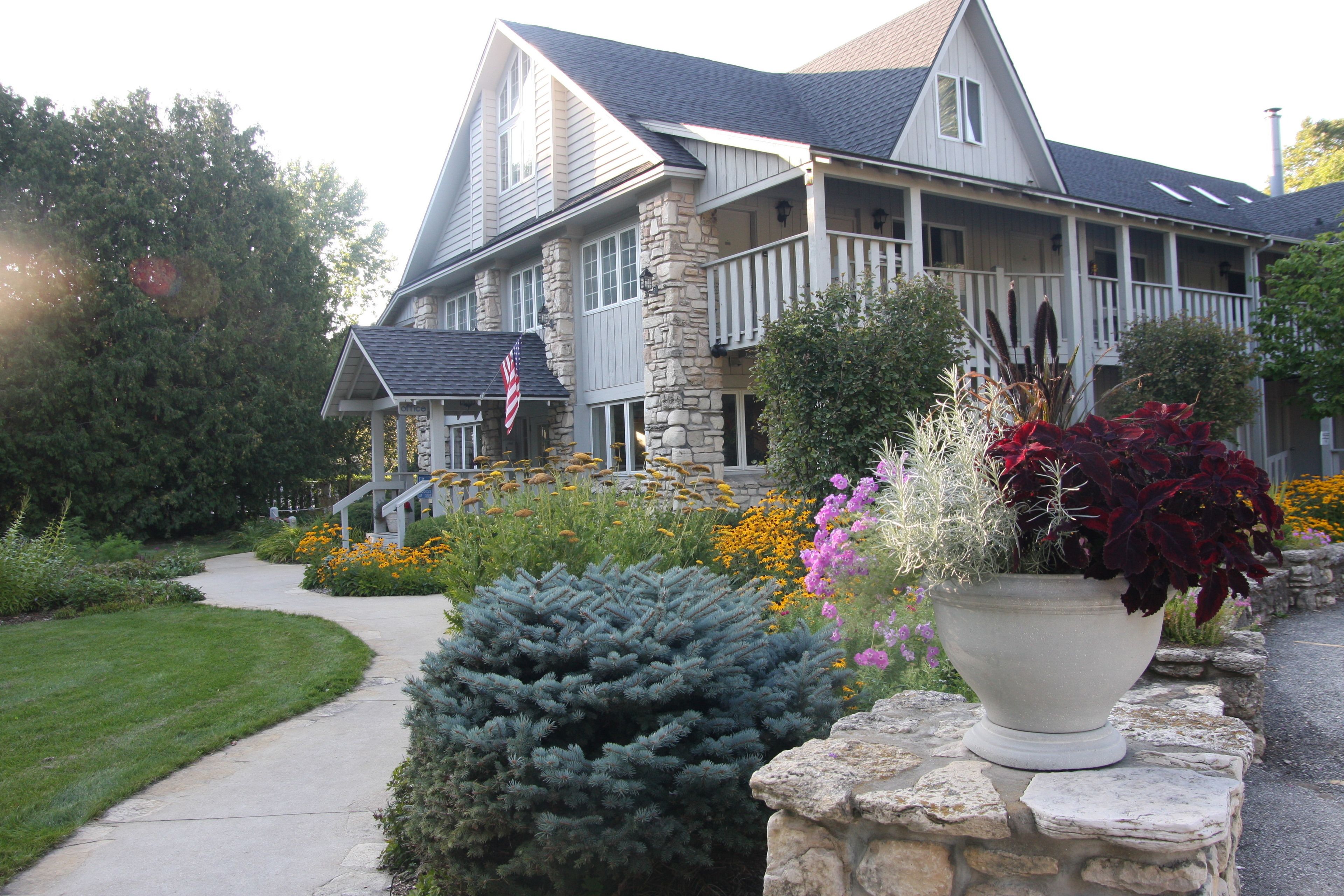 A large stone house with a porch, surrounded by a well-maintained garden with various plants and flowers.