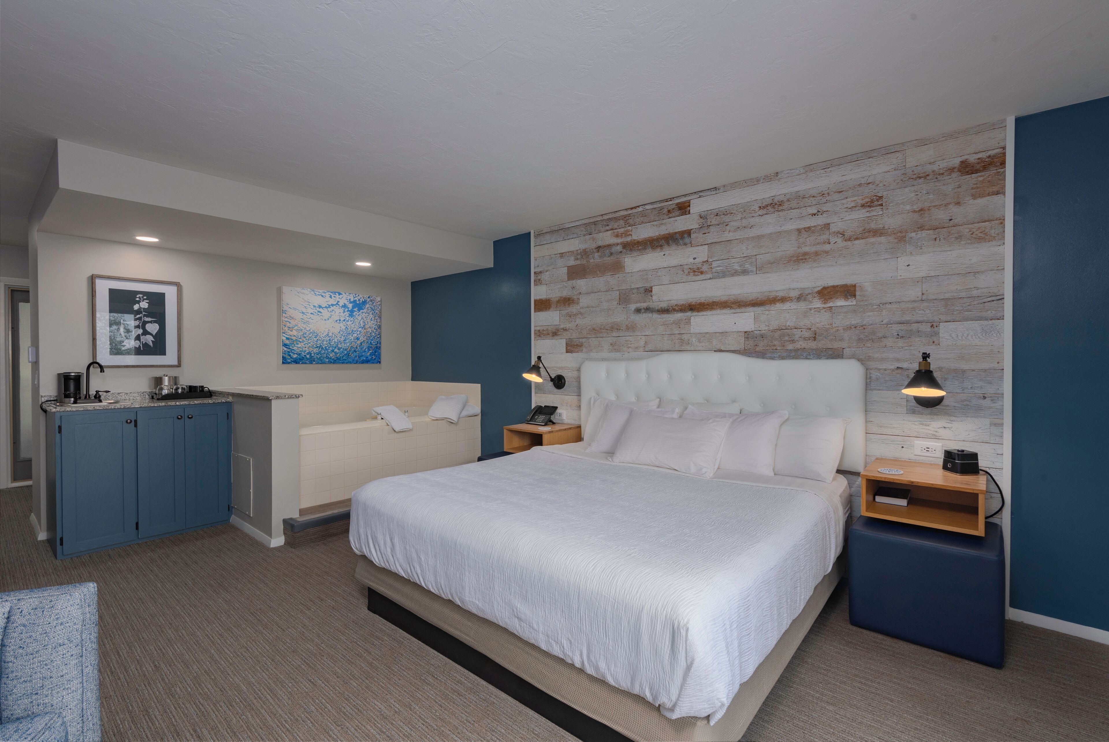 Une chambre moderne avec un grand lit, un bureau intégré, un canapé et un mur d’accent en bois.