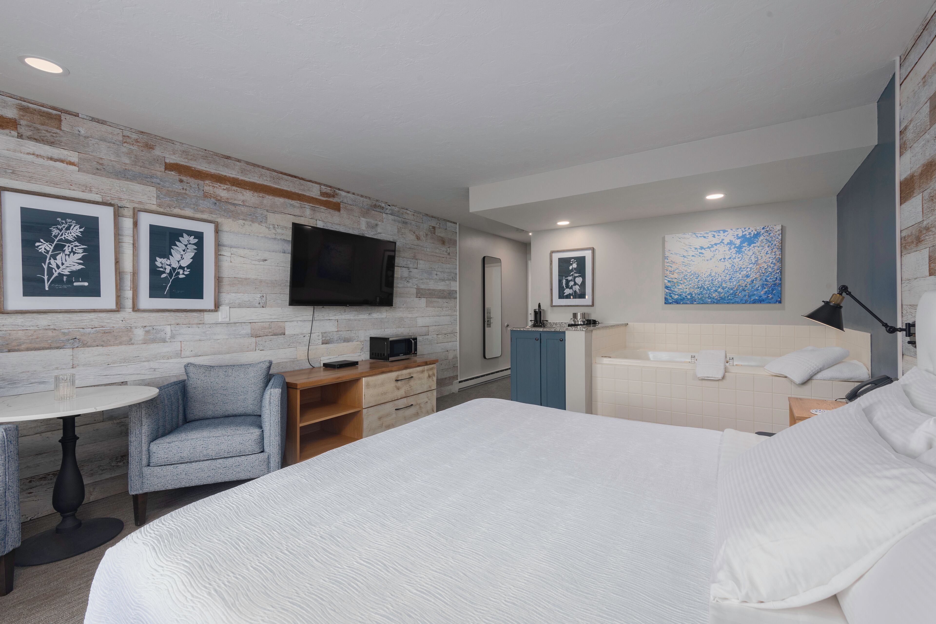 Une chambre d’hôtel moderne dotée d’un grand lit, d’un bureau avec une chaise, d’un téléviseur à écran plat, d’un four à micro-ondes, d’une armoire bleue, d’une baignoire et d’œuvres d’art accrochées aux murs.