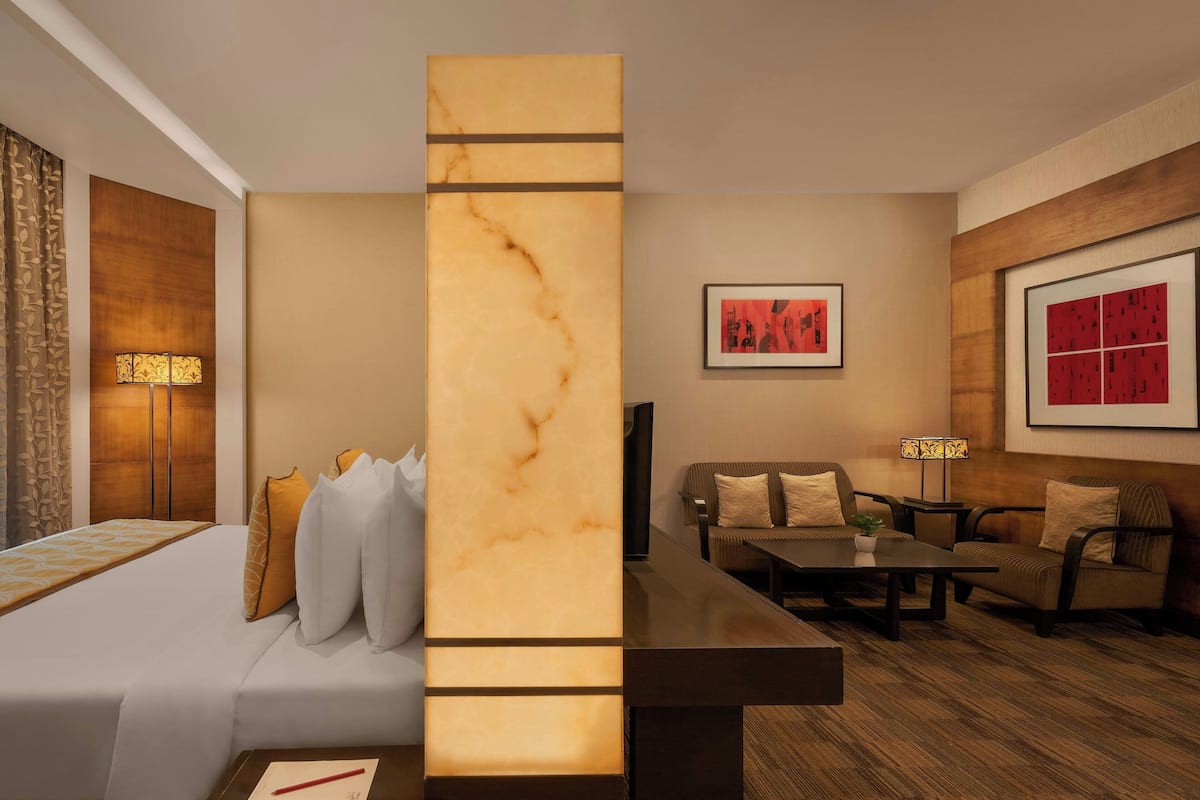 A modern hotel room with a large bed, a sofa, a coffee table, and two floor lamps.
