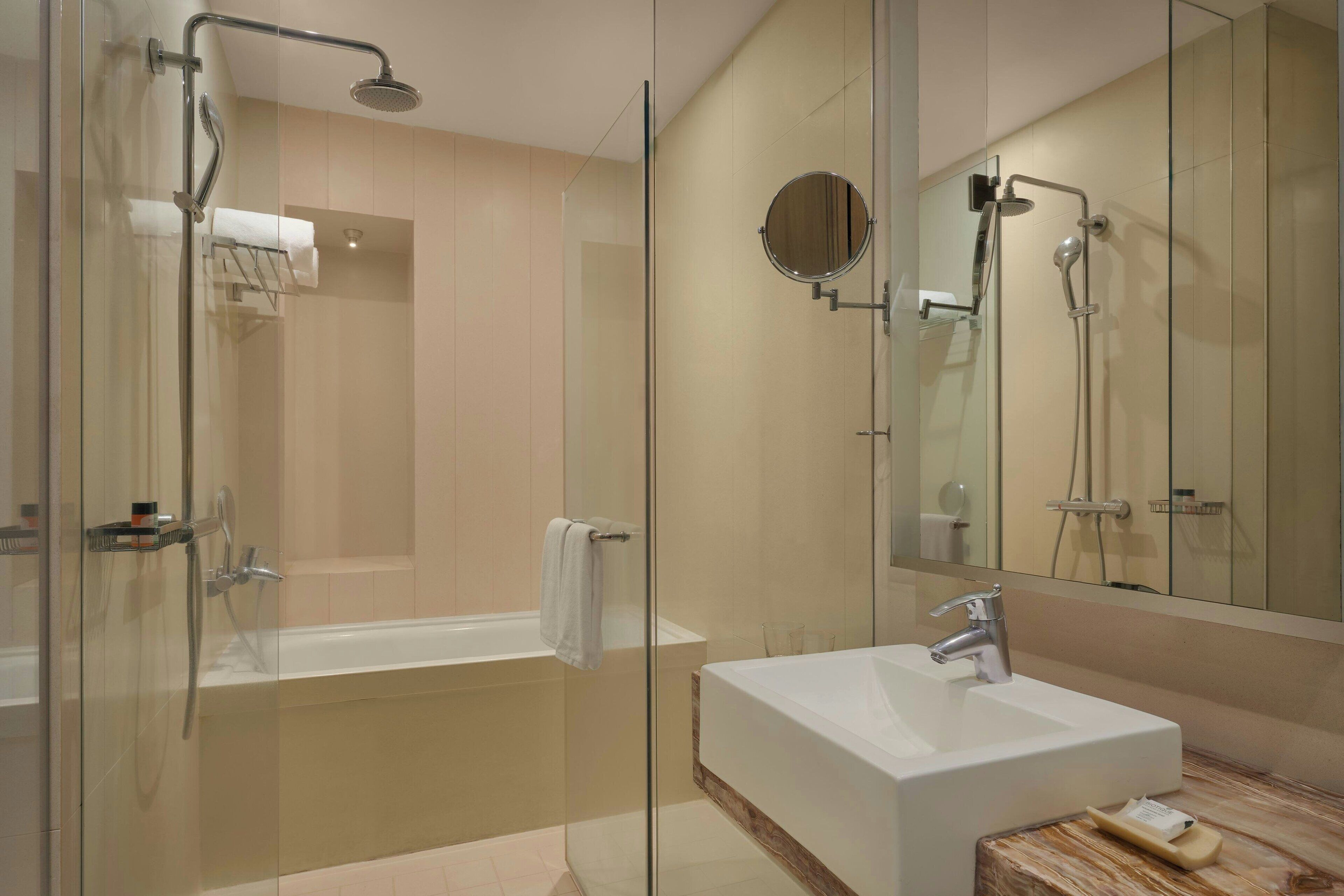 A modern bathroom with a glass-enclosed shower, a standalone bathtub, and a large mirror above the sink.