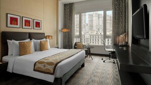A hotel room with a large bed, a desk, a chair, a TV, and a view of tall buildings. - Meluha The Fern Mumbai, Powai, Series by Marriott (Mumbai)