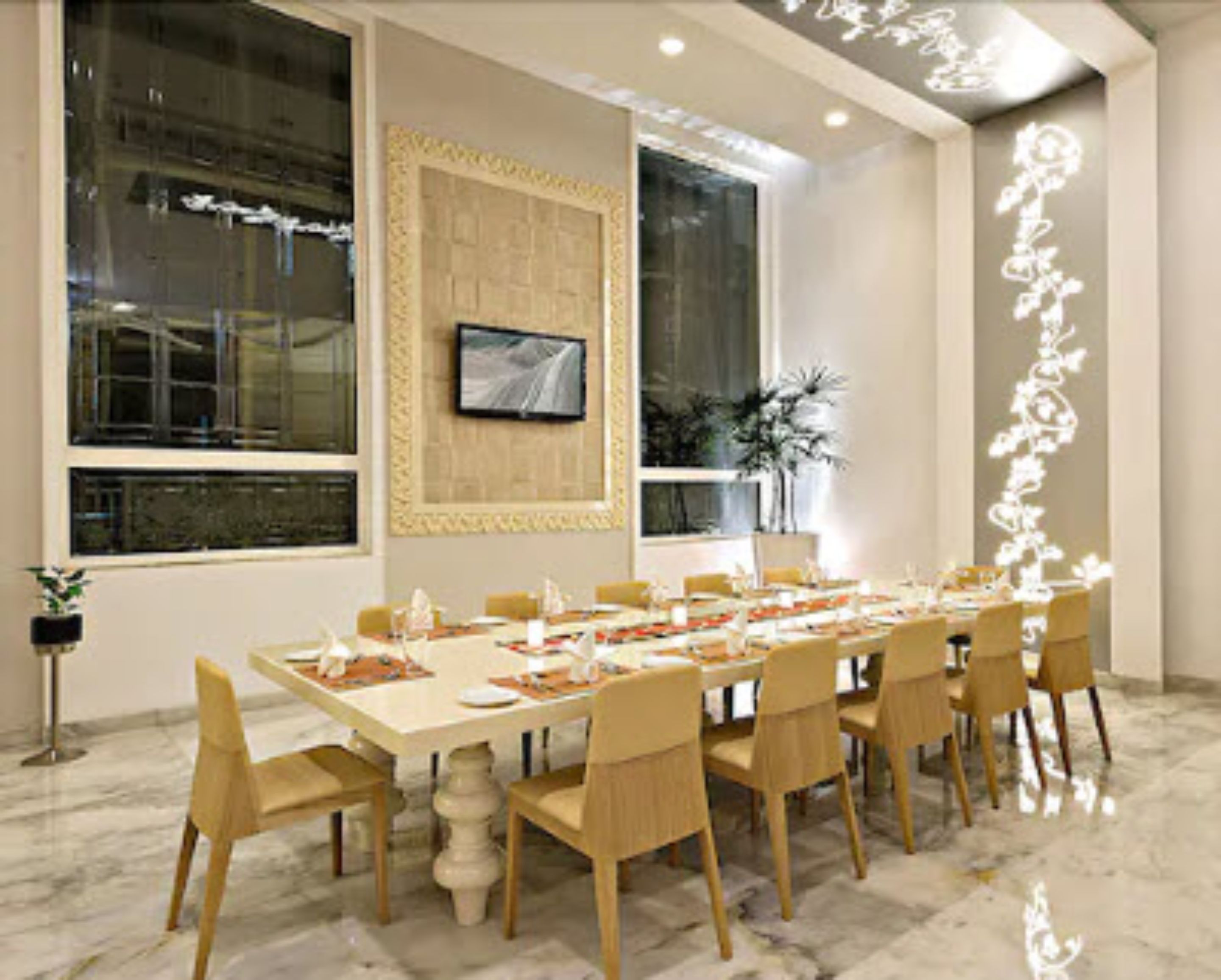 A spacious dining area with a long table set for multiple guests, large windows, and a flat-screen TV mounted on the wall.