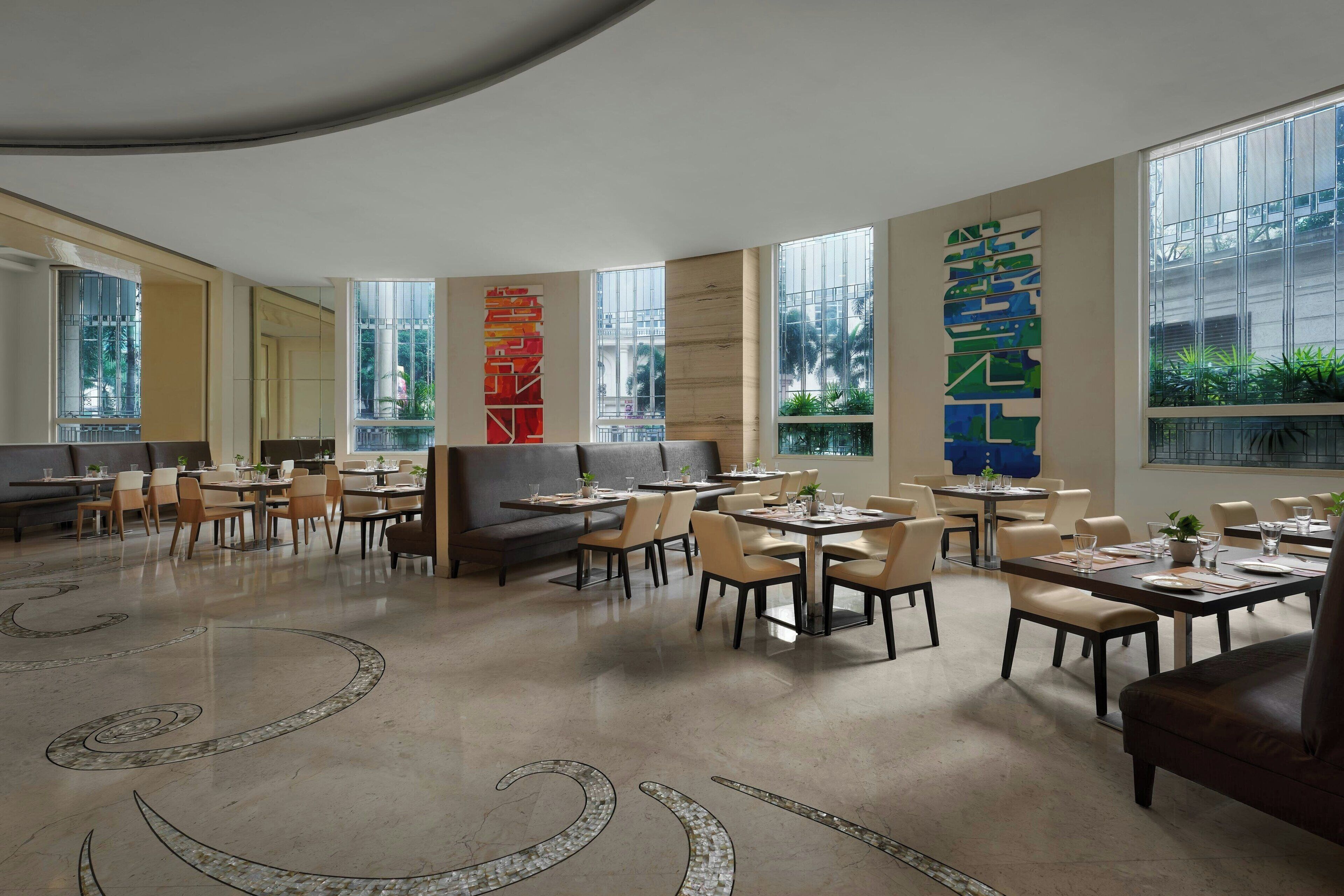 A spacious dining area with multiple tables and chairs, large windows, and decorative wall art.