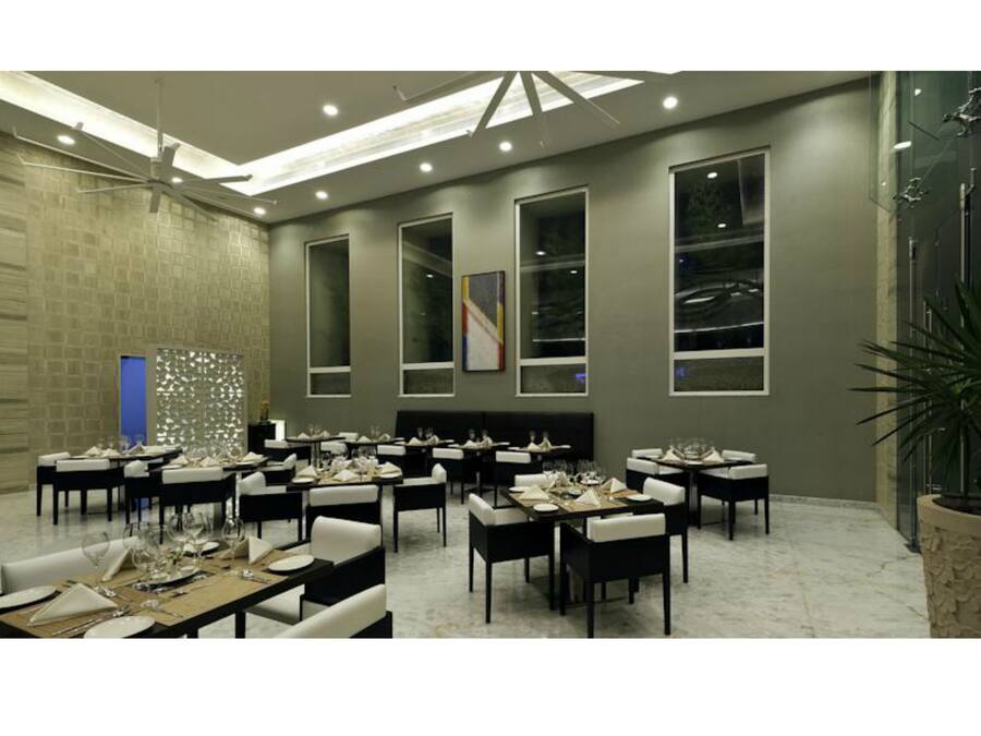 Un comedor moderno con varias mesas y sillas, ventanas amplias e iluminación empotrada en el techo.