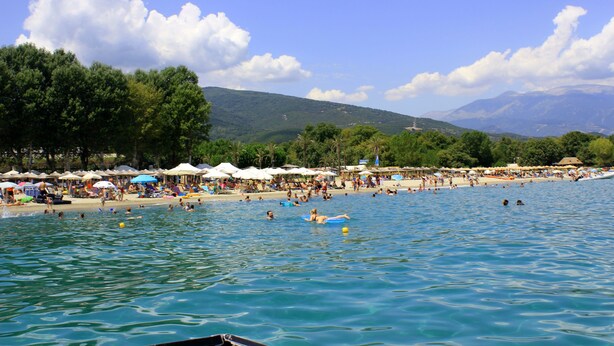 A beach with people swimming and sunbathing, umbrellas, and a mountainous backdrop. - Zeus Hotel (Dio-Olympos)