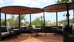 A covered outdoor seating area with tables and chairs, a sofa, and a grill. - Zeus Hotel (Dio-Olympos)