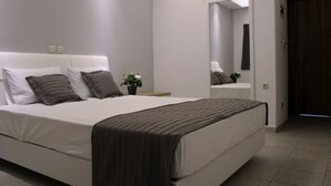 A modern bedroom with a large bed, white walls, and a dark wooden door. - Zeus Hotel (Dio-Olympos)