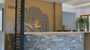 A reception desk with a stone facade, a wooden panel on the left, and a plant on the right. - Zeus Hotel (Dio-Olympos)