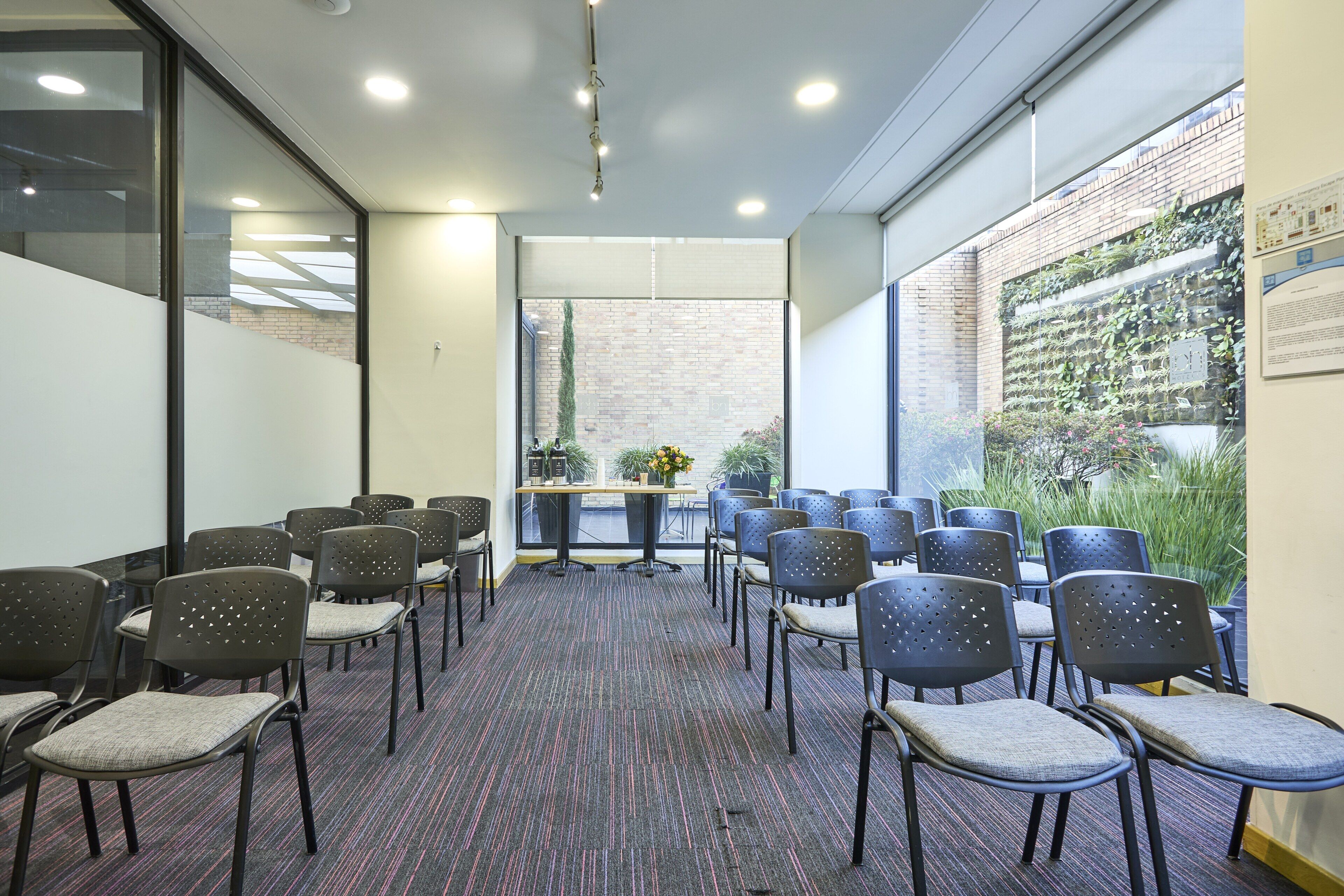 Un salón de conferencias con filas de sillas, piso alfombrado y una pared de ladrillo con plantas.