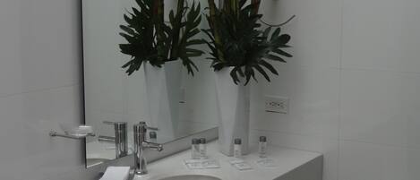 A modern bathroom with a white sink, mirror, and two vases with red flowers.