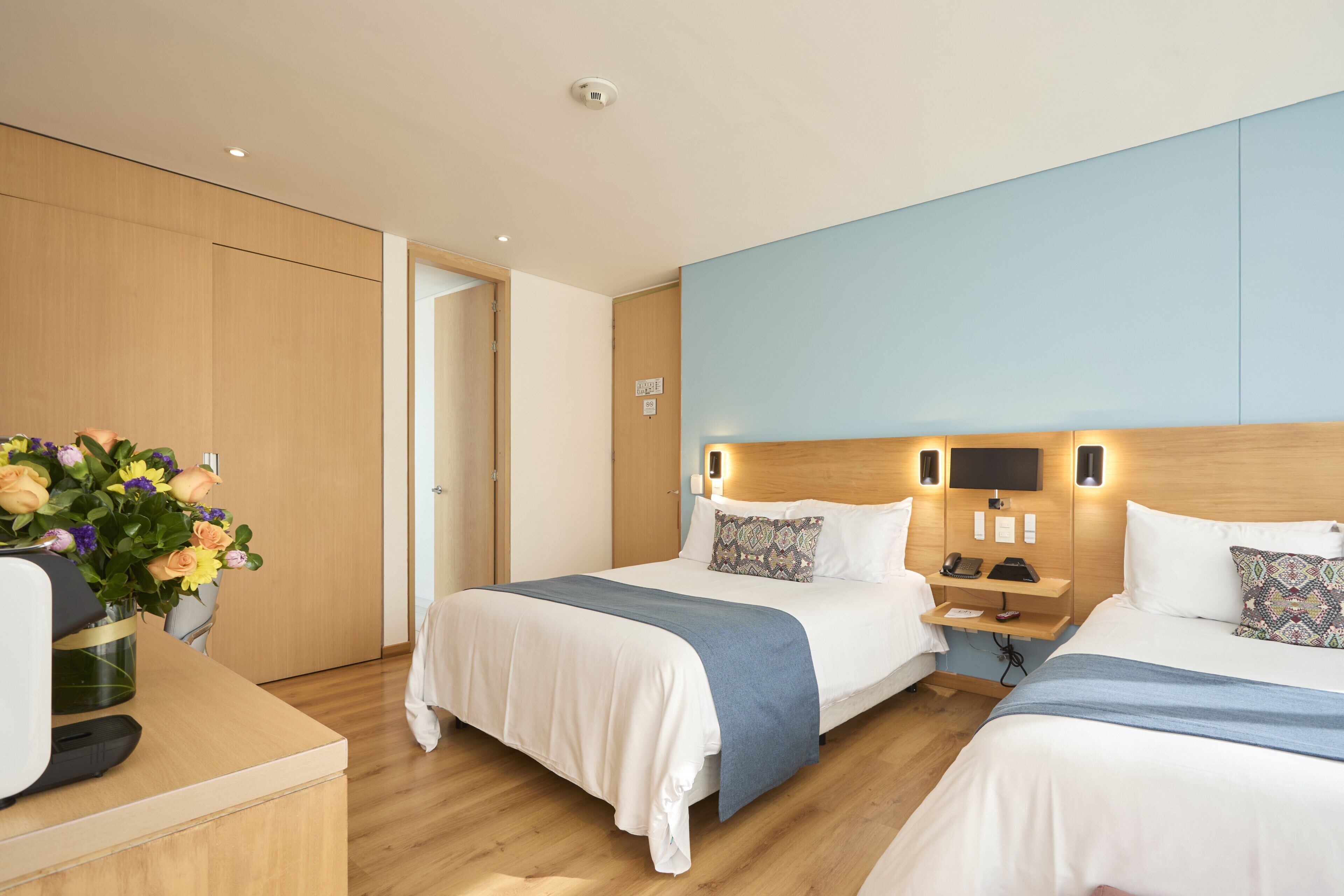 A hotel room with two beds, a desk, and a vase of flowers.