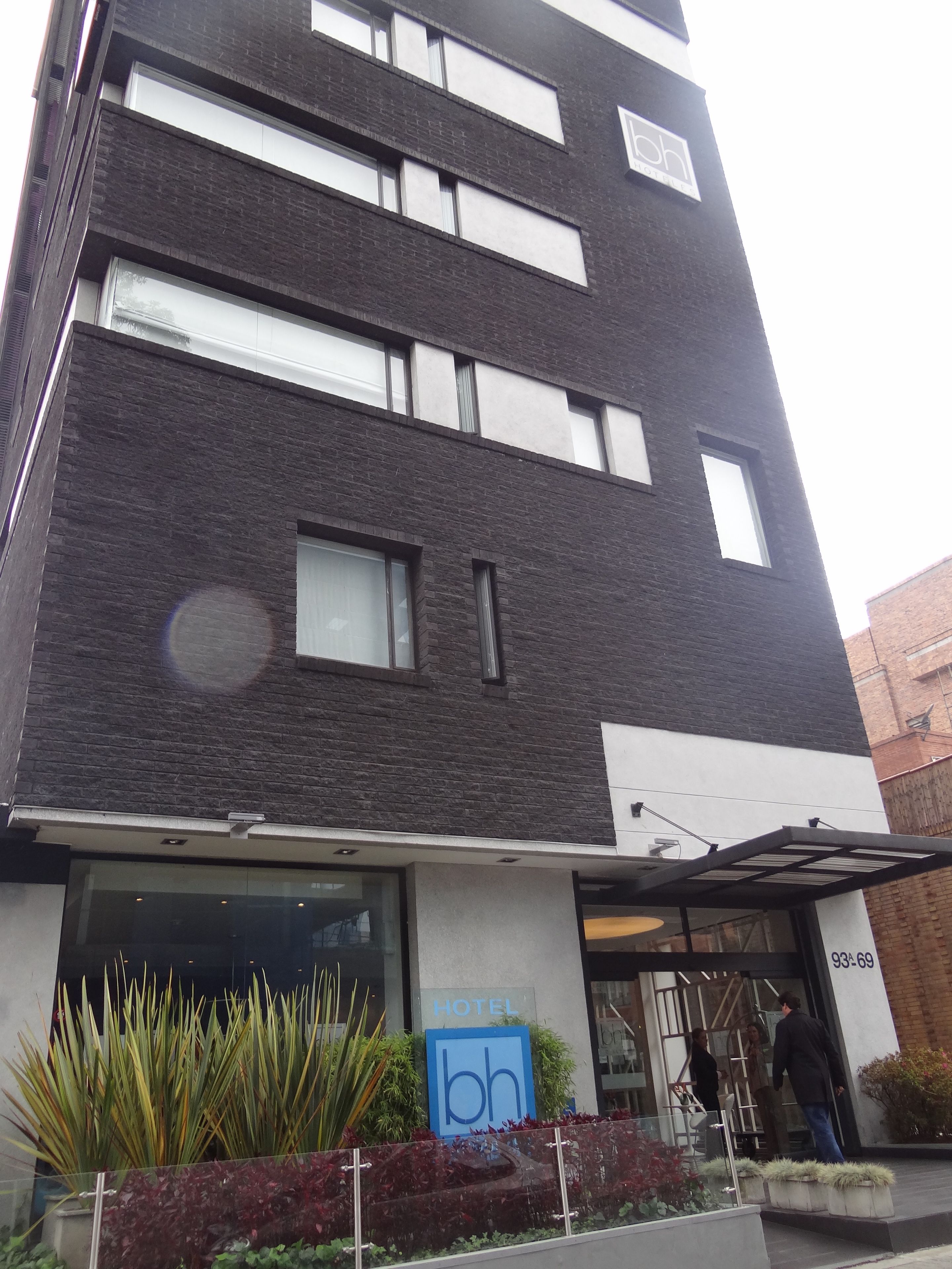 A modern hotel with a dark brick facade, large windows, and a blue sign with 'bh' logo.