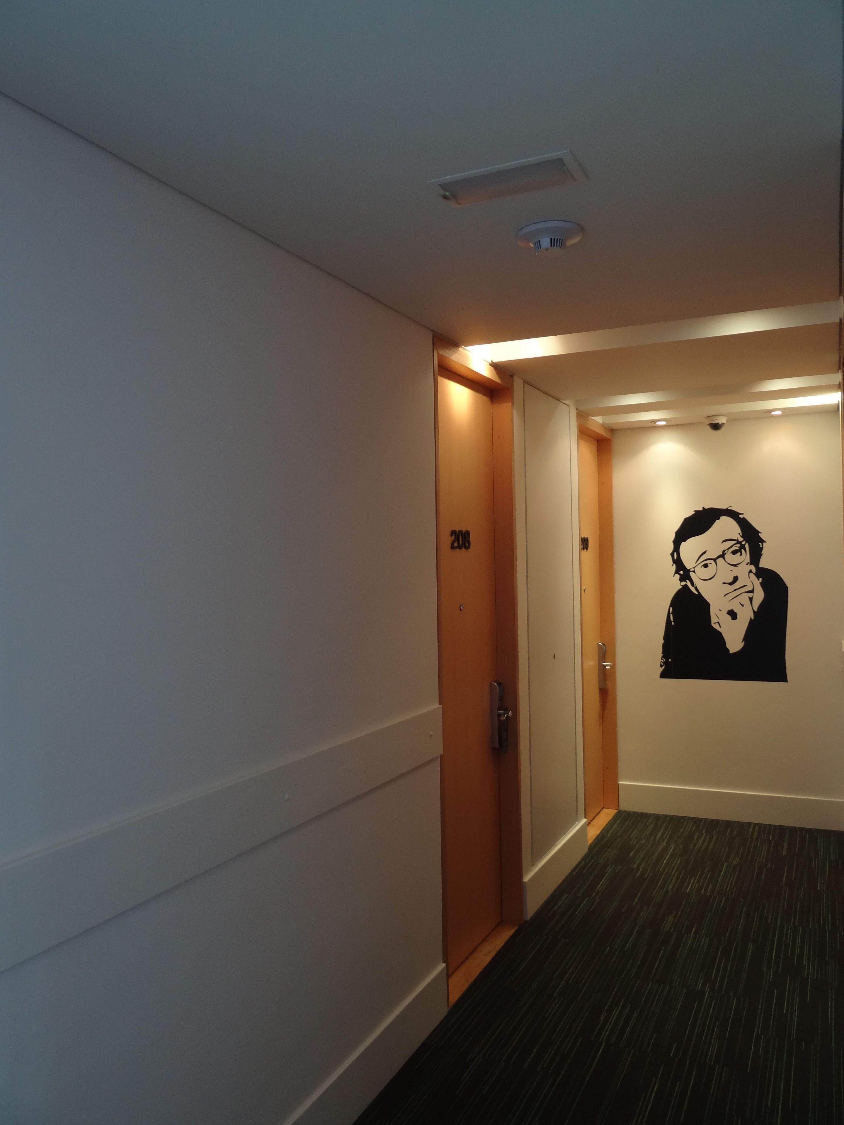 A hallway with a door marked '208', a black and white wall decal, and a ceiling light.