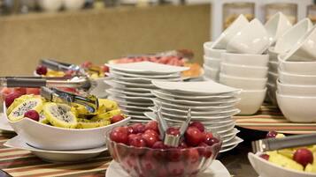 Una mesa de buffet con varias frutas y platos apilados.