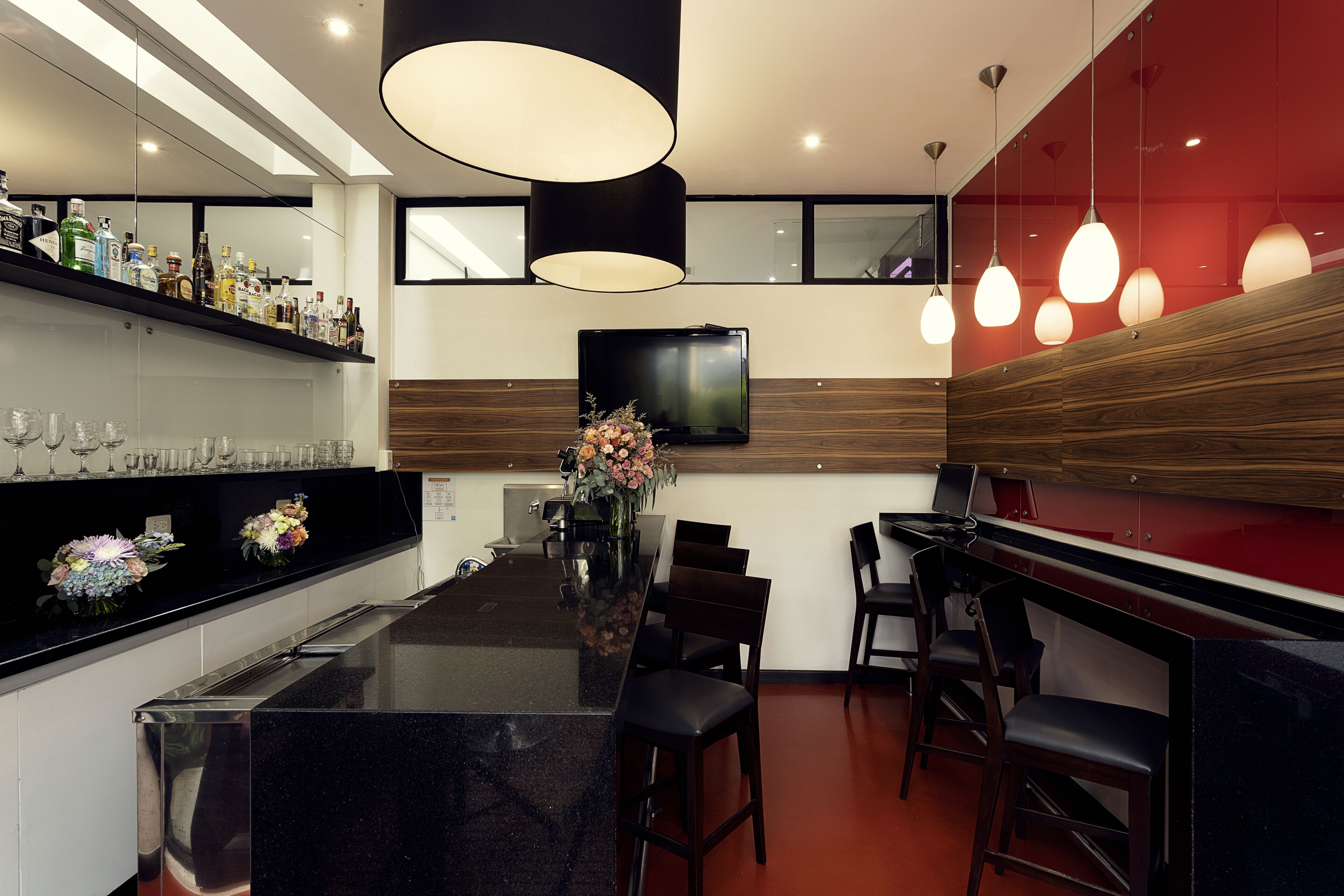 Un espace bar moderne avec un comptoir noir, des éléments décoratifs en bois et un téléviseur à écran plat fixé au-dessus du bar.