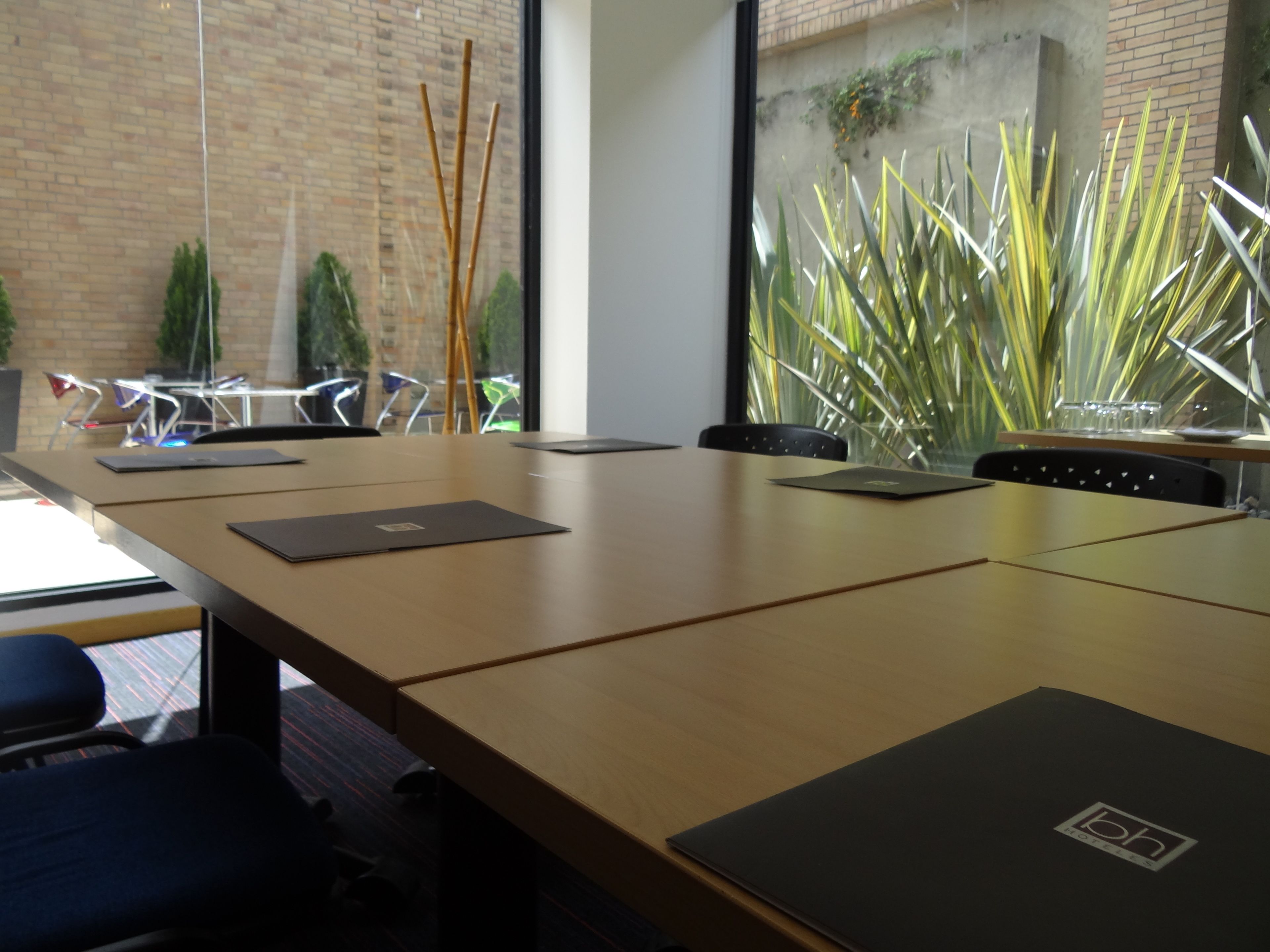 A conference room with a long table, chairs, and a view of a brick wall and plants.