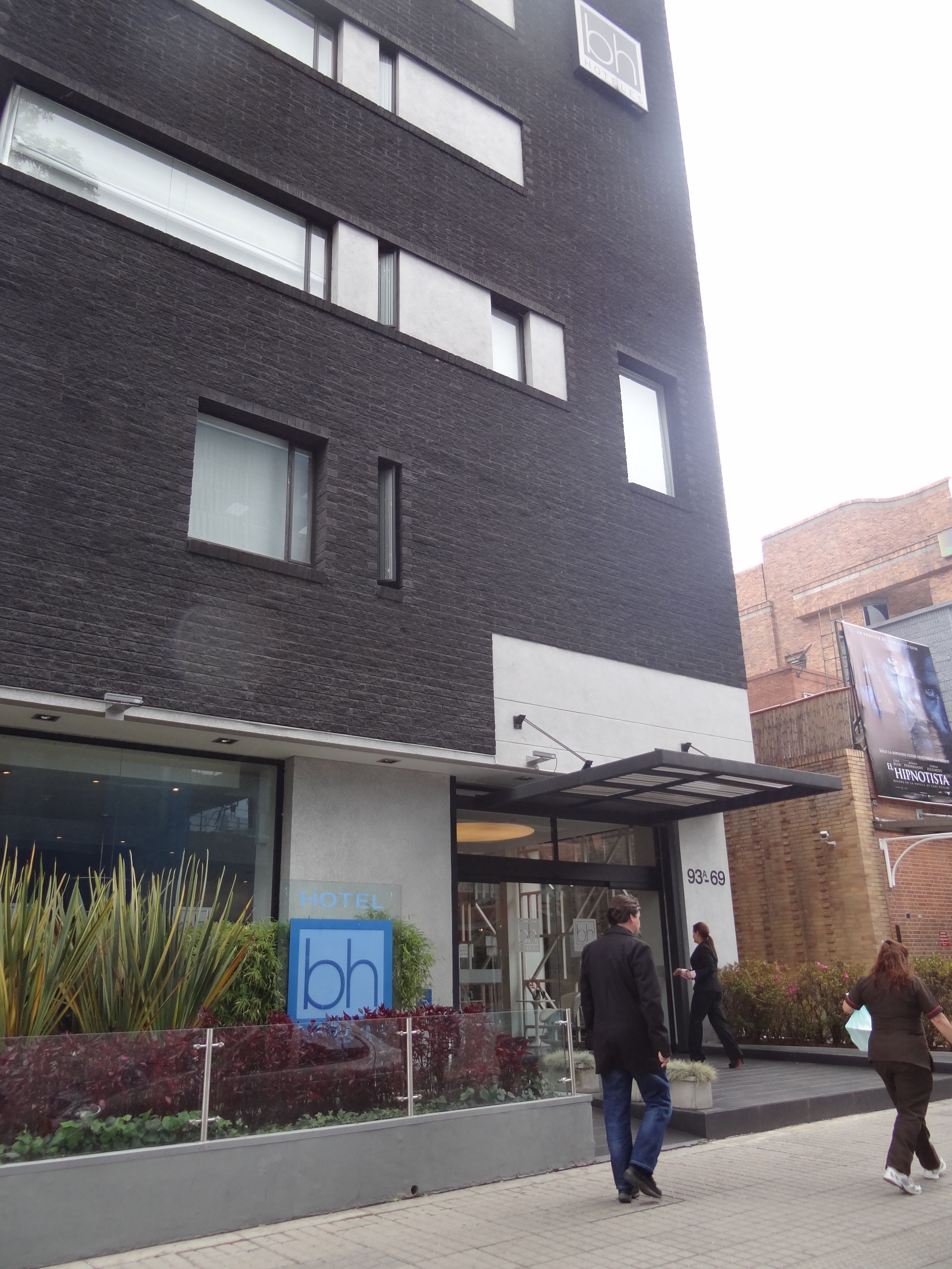 A modern hotel with a glass facade, a sign indicating it is a 'HOTEL', and a visible entrance.