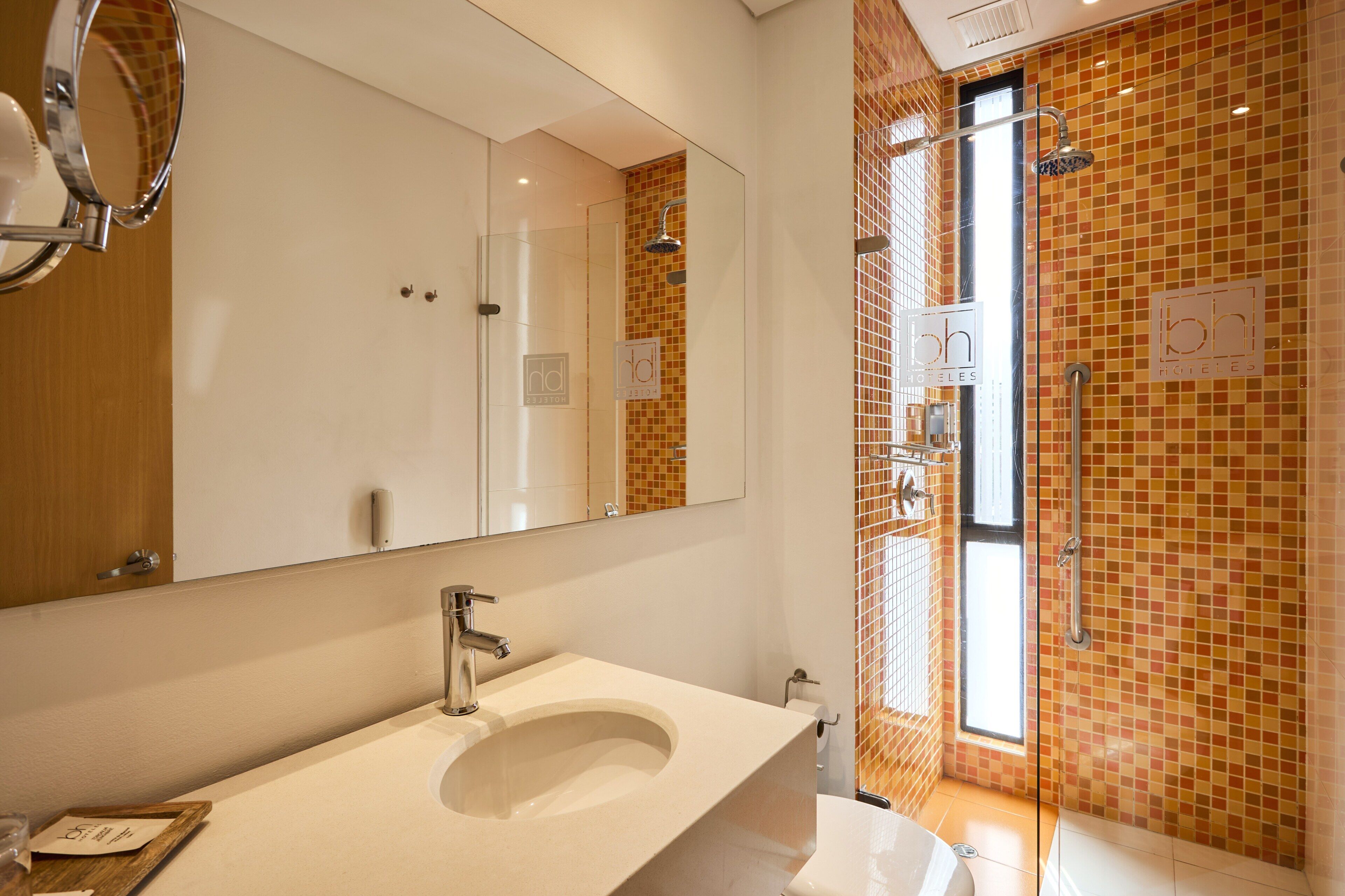 Un baño moderno con un espejo grande, un lavabo y una zona de ducha con puerta de cristal.