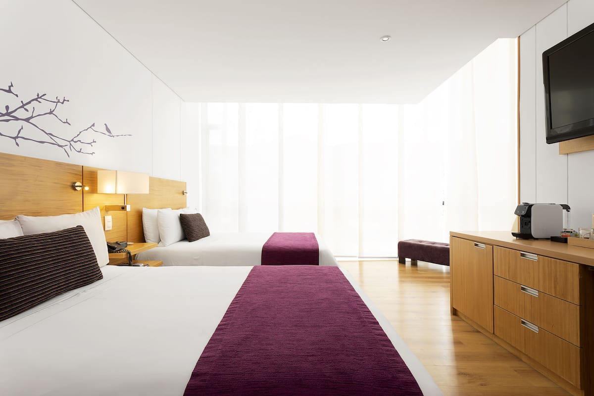 A modern hotel room with a large bed, a wooden headboard, a TV, and a small kitchenette.