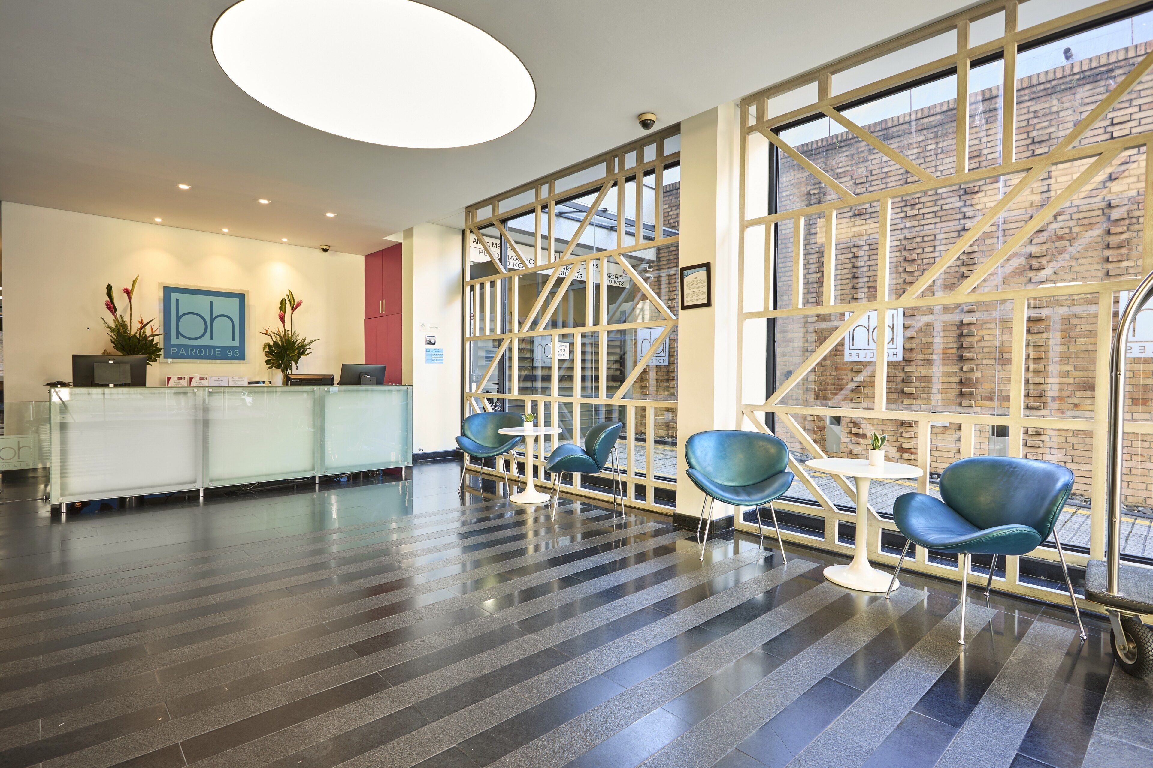 A modern hotel lobby with a reception desk, seating area, and large windows offering views of the city.
