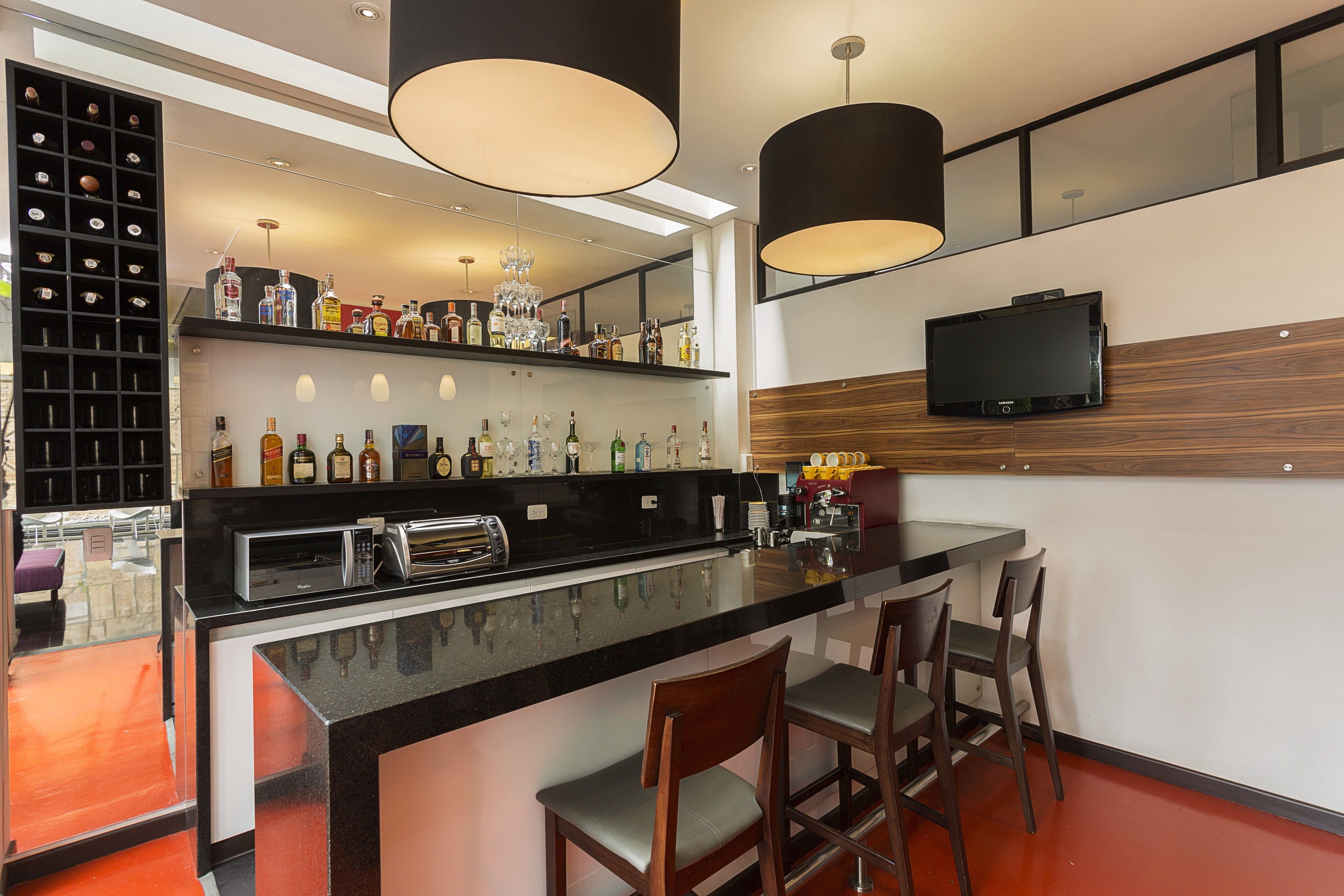 Eine moderne Bar mit einer schwarzen Arbeitsplatte, Barhocker, einem Weinkühler und einem an der Wand befestigten Fernseher.