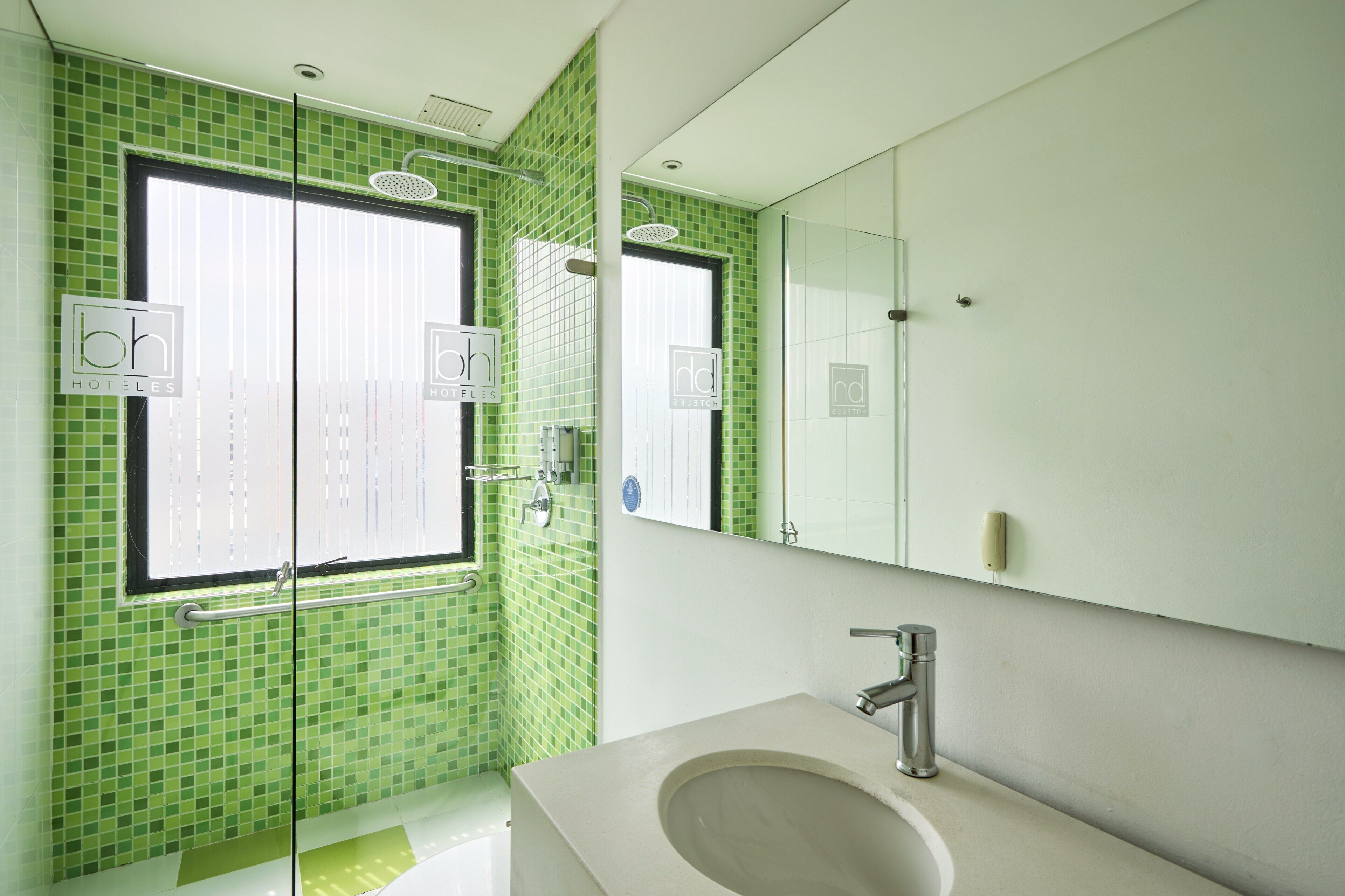Un bagno con piastrelle a mosaico verdi, un lavandino con un rubinetto moderno e uno specchio sopra.