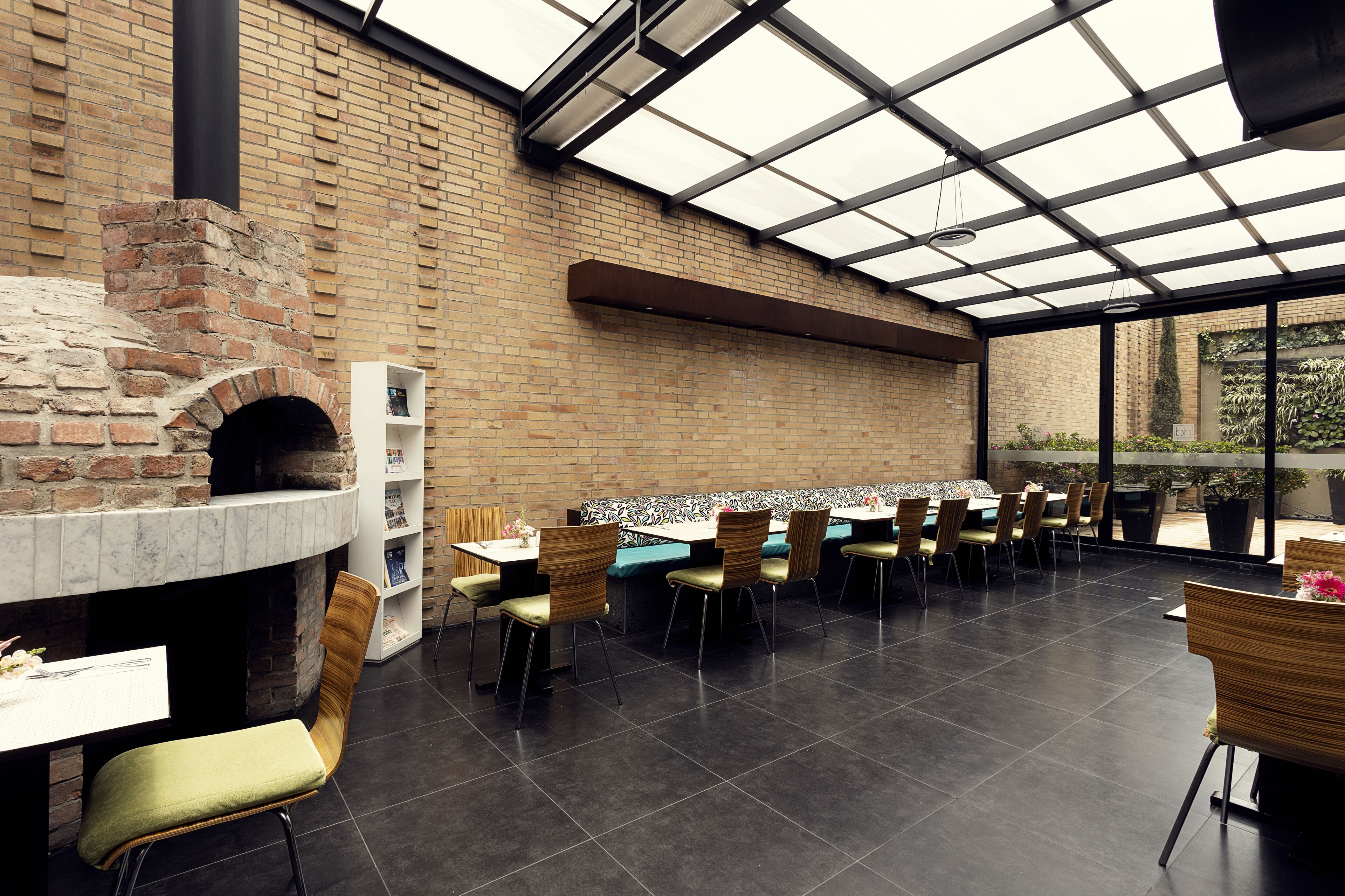 A restaurant with a brick oven, outdoor seating, and a glass ceiling.