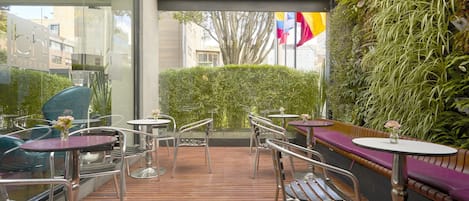 An outdoor seating area with metal chairs and tables, a wooden deck, and a green vertical garden wall.