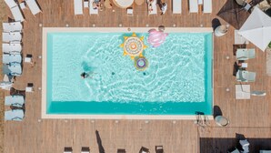 Vue aérienne d’une piscine rectangulaire entourée d’une terrasse en bois, avec des chaises longues et des parasols.