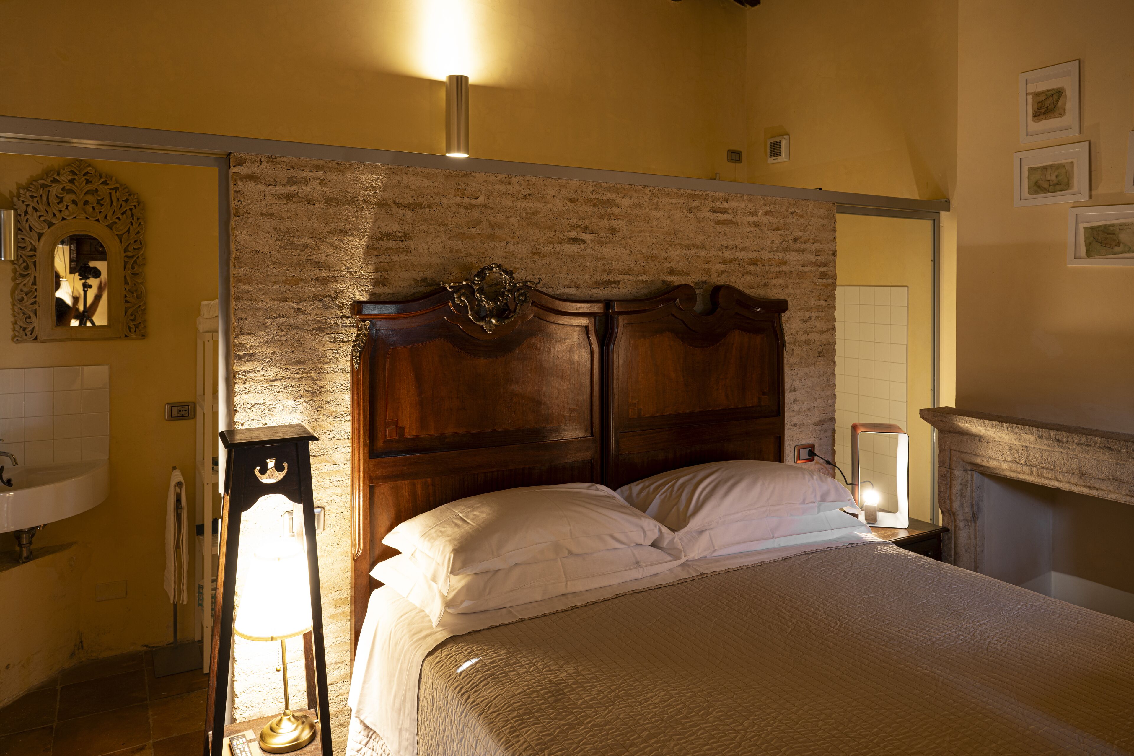 A bedroom with a wooden headboard, a bedside table with a lamp, and a view of the bathroom.