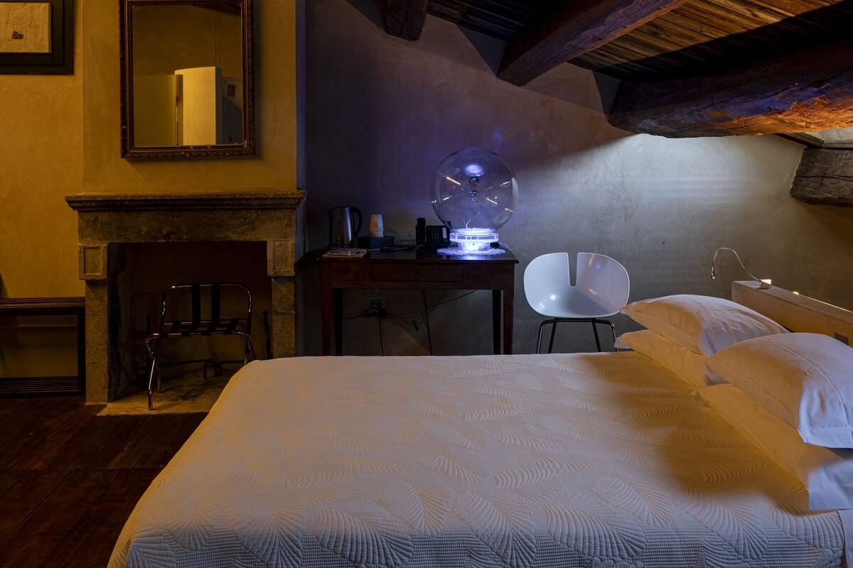 A bedroom with a large bed, a desk, a chair, a fireplace, and a mirror.