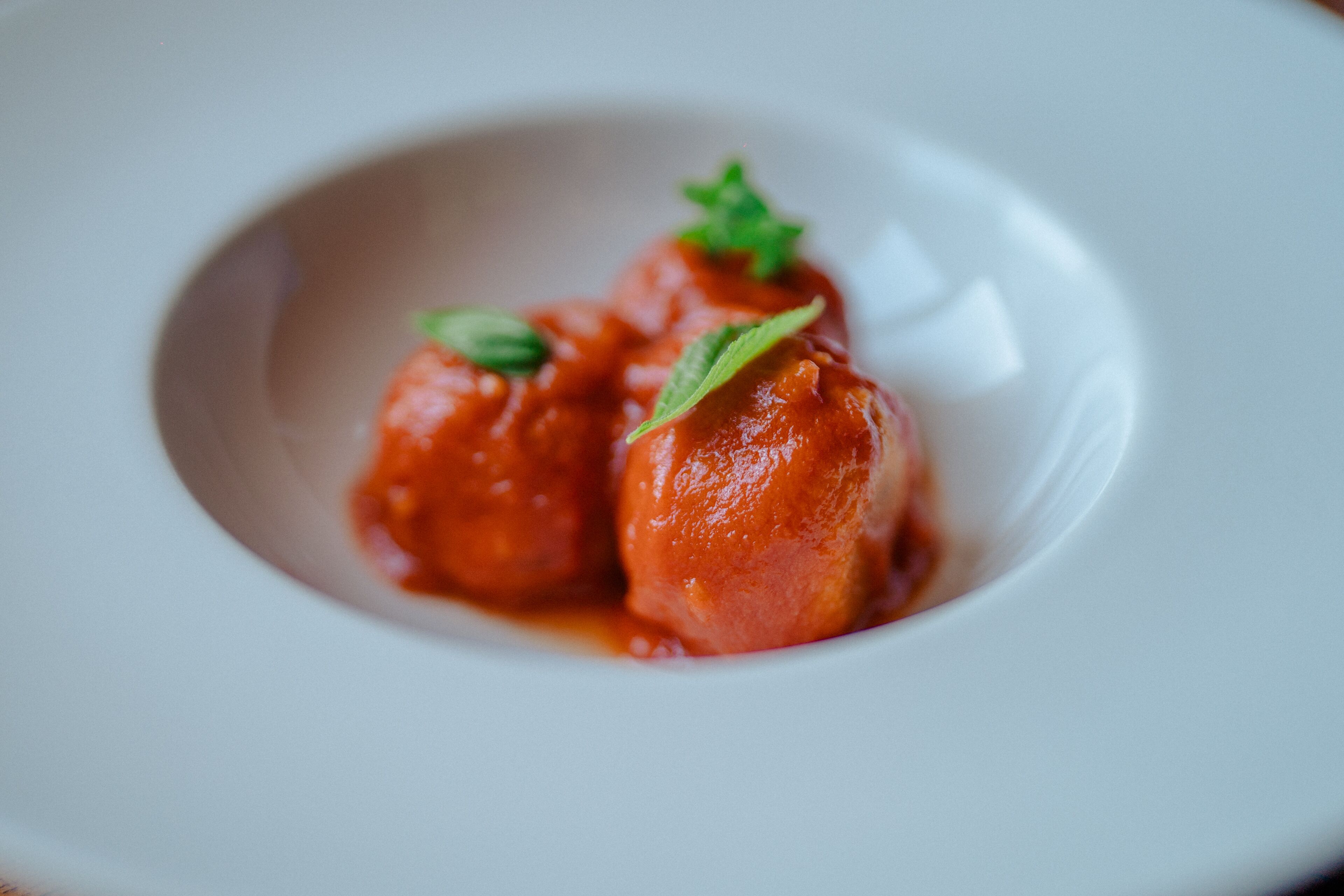 Une assiette blanche contenant deux boulettes rondes, recouvertes d’un glaçage rouge, et décorées de feuilles vertes.