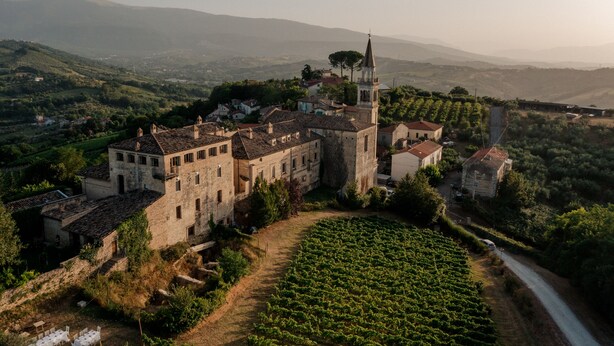 Un bâtiment historique doté d’une tour imposante, entouré de vignobles luxuriants et de collines ondoyantes.