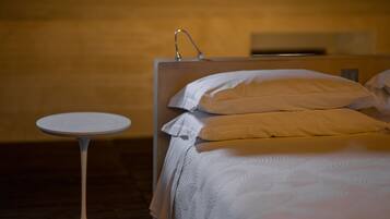 Ein ordentlich bezogenes Bett mit weißer und beiger Bettwäsche, ein kleiner runder Tisch und ein wandmontierter Waschtisch.