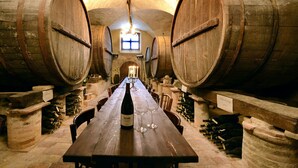 Une longue table en bois, avec une bouteille de vin et des verres au centre, flanquée de piliers en pierre et de barils en bois.