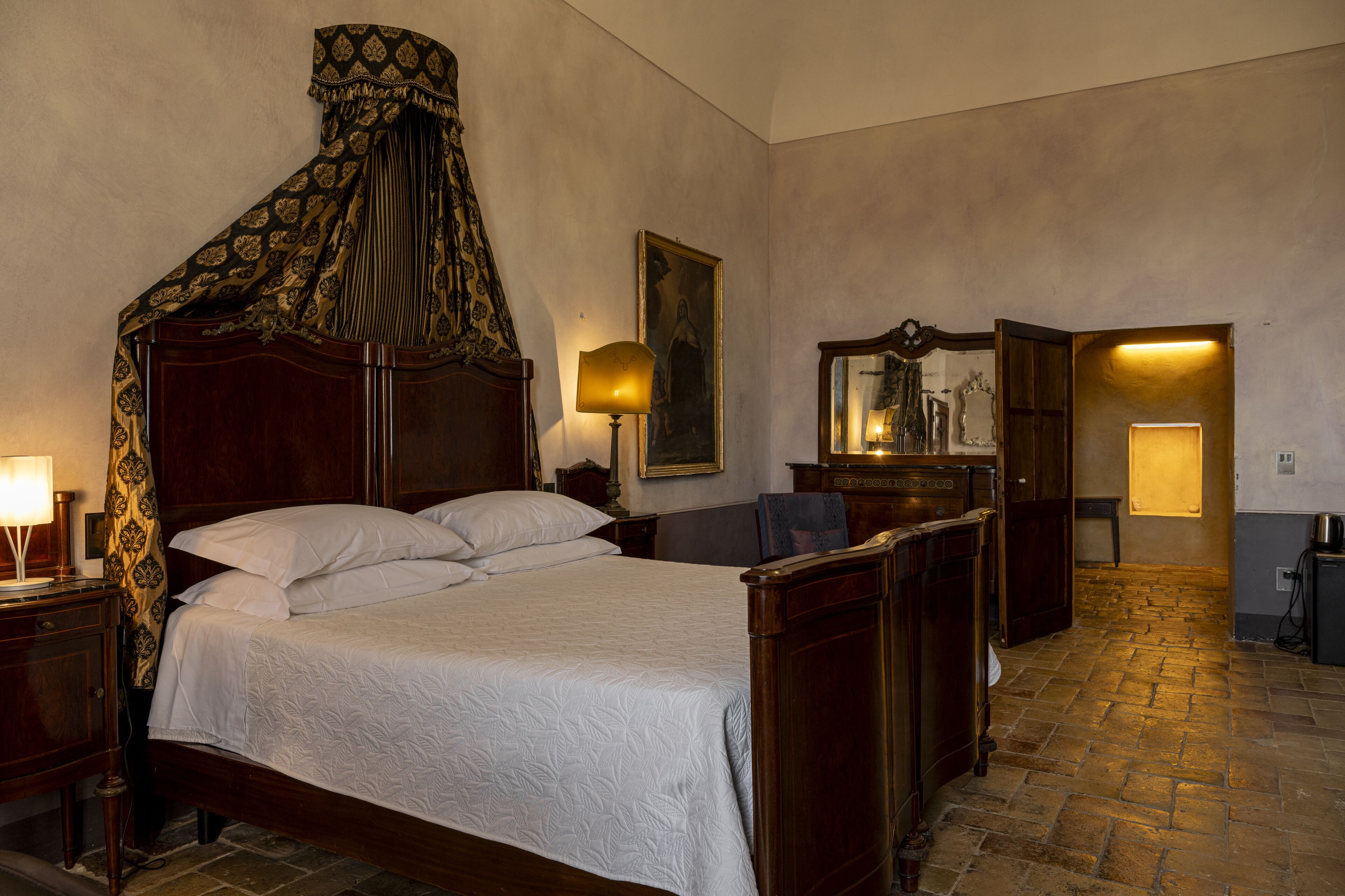 Une chambre à coucher de style traditionnel, avec un lit à baldaquin, une armoire en bois, un miroir et une petite table avec une lampe.