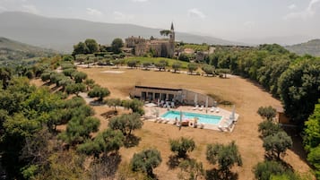 Una grande villa con piscina, circondata da ulivi e con vista su un edificio storico in lontananza.