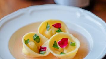 A plate of ravioli with a sauce and garnishes, a bottle of wine, and a teapot in the background.